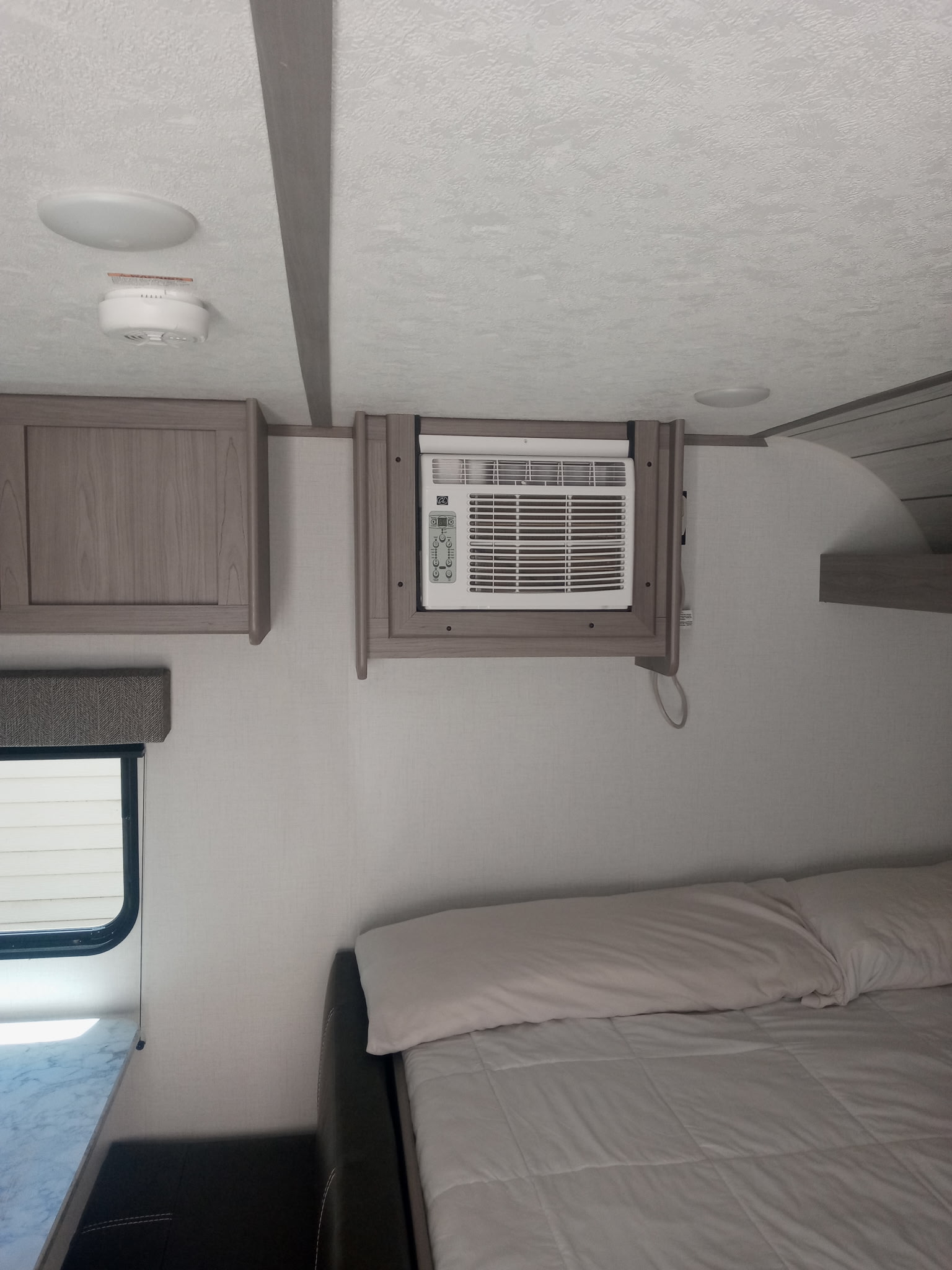 Modern RV rental interior with a wall-mounted AC unit above a comfortable bed and wooden cabinets, highlighting a compact bedroom.. Coleman Lantern LT 2023