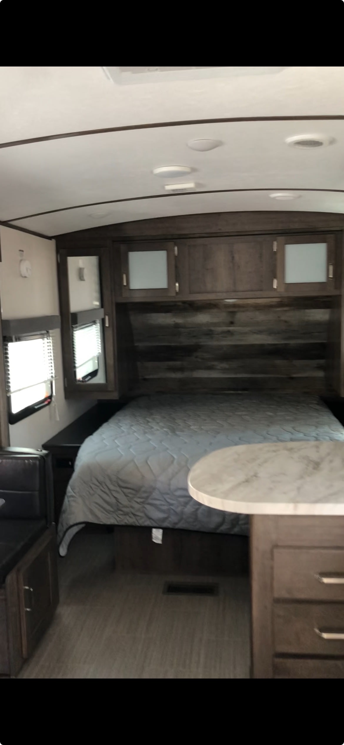 Step inside this RV rental's bedroom. It features a bed with wood-paneled headboard, overhead cabinets, and a dining nook.. Keystone RV Passport Grand Touring 2020