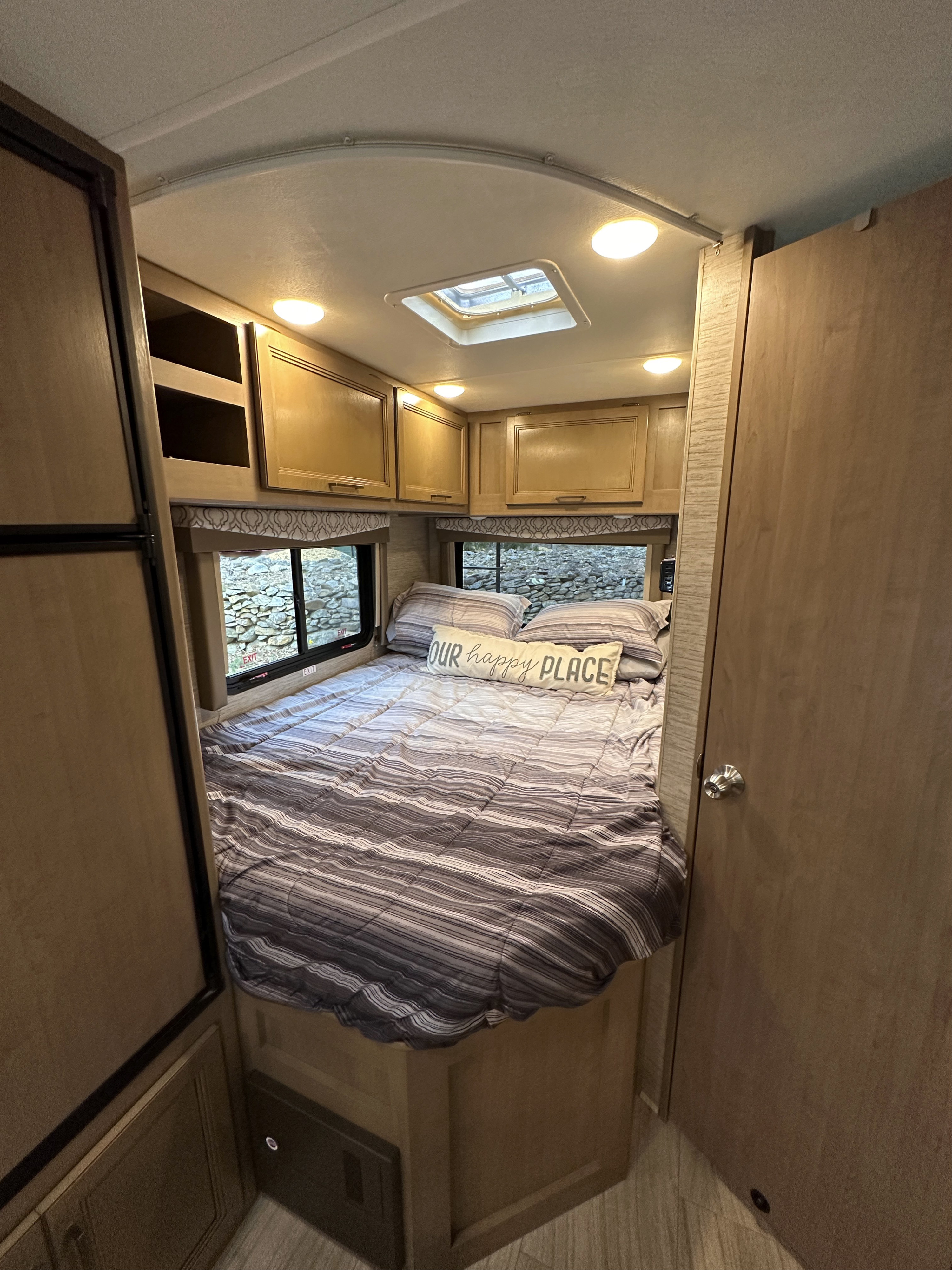 Cozy RV rental bedroom with striped bedding, overhead cabinets, and a skylight for natural light.. Thor Quantum SE 2021
