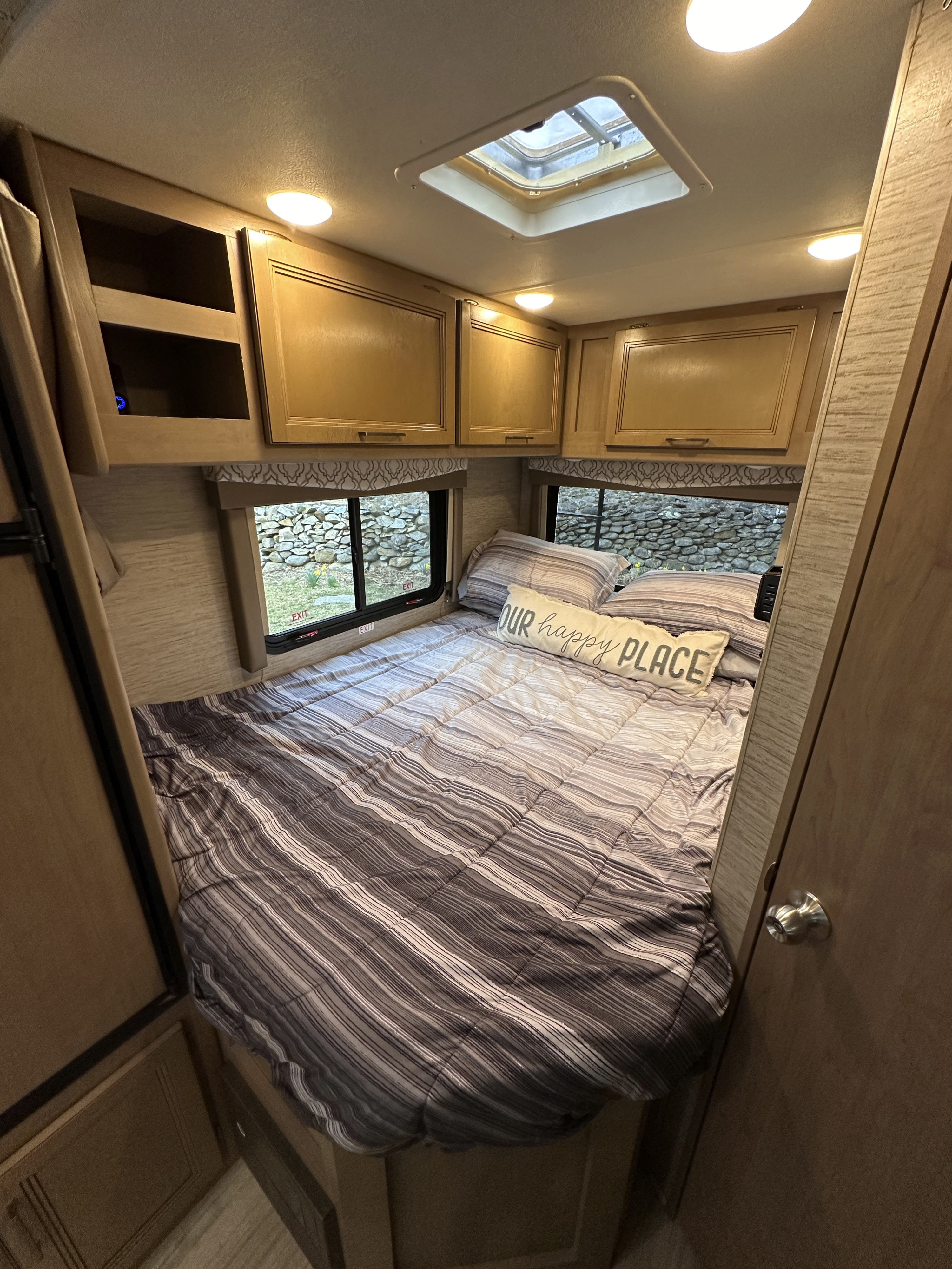 Cozy RV bedroom for your next rv rental. Features striped bedding, windows, and overhead cabinets.. Thor Quantum SE 2021