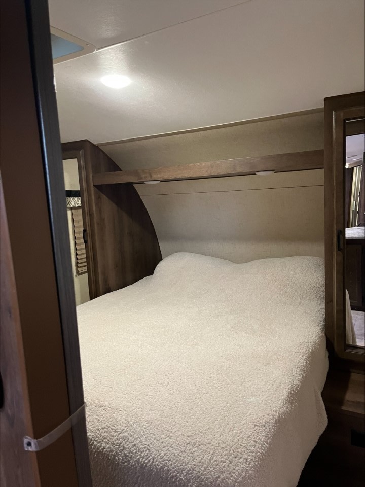 Inside an RV rental: a cozy bedroom with a fluffy white bed, overhead lighting, and wood cabinetry.. KZ Connect 2018