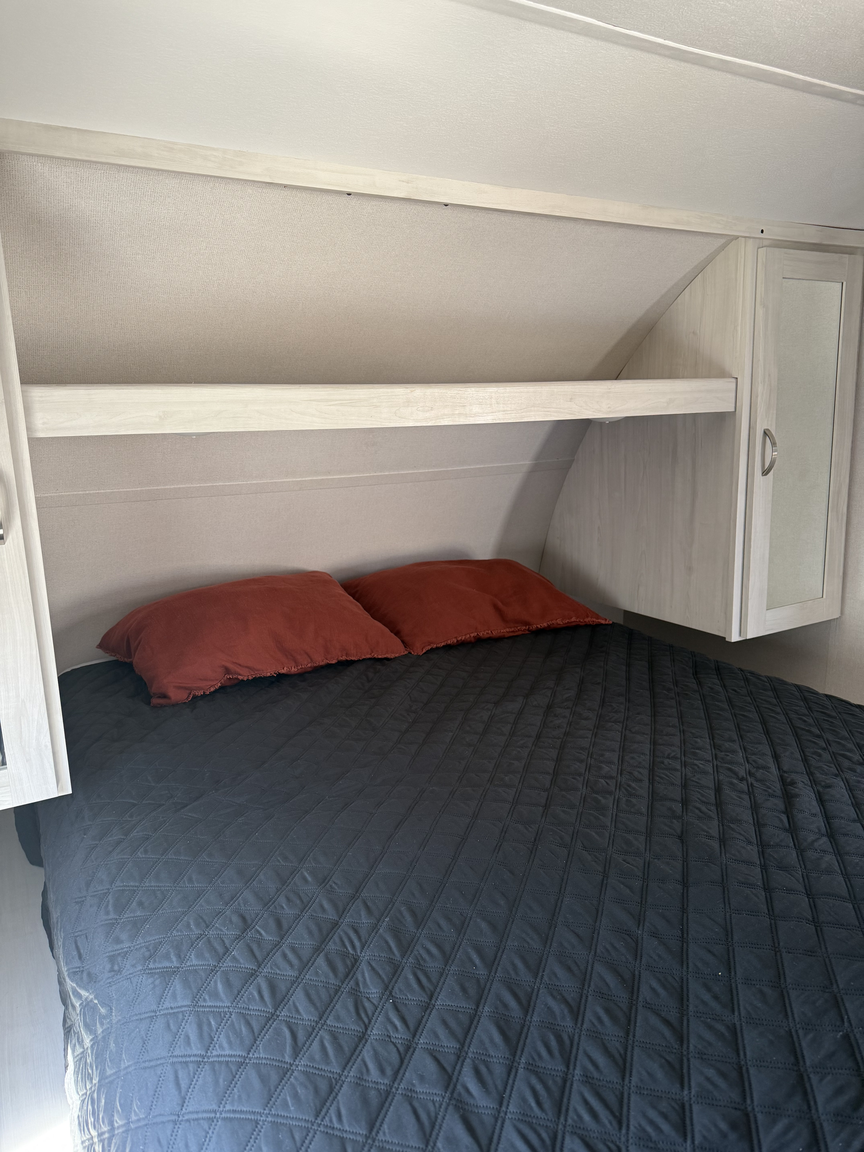 Cozy RV rental bedroom with a dark quilted comforter, red pillows, and overhead storage.. Primetime Tracer 2022