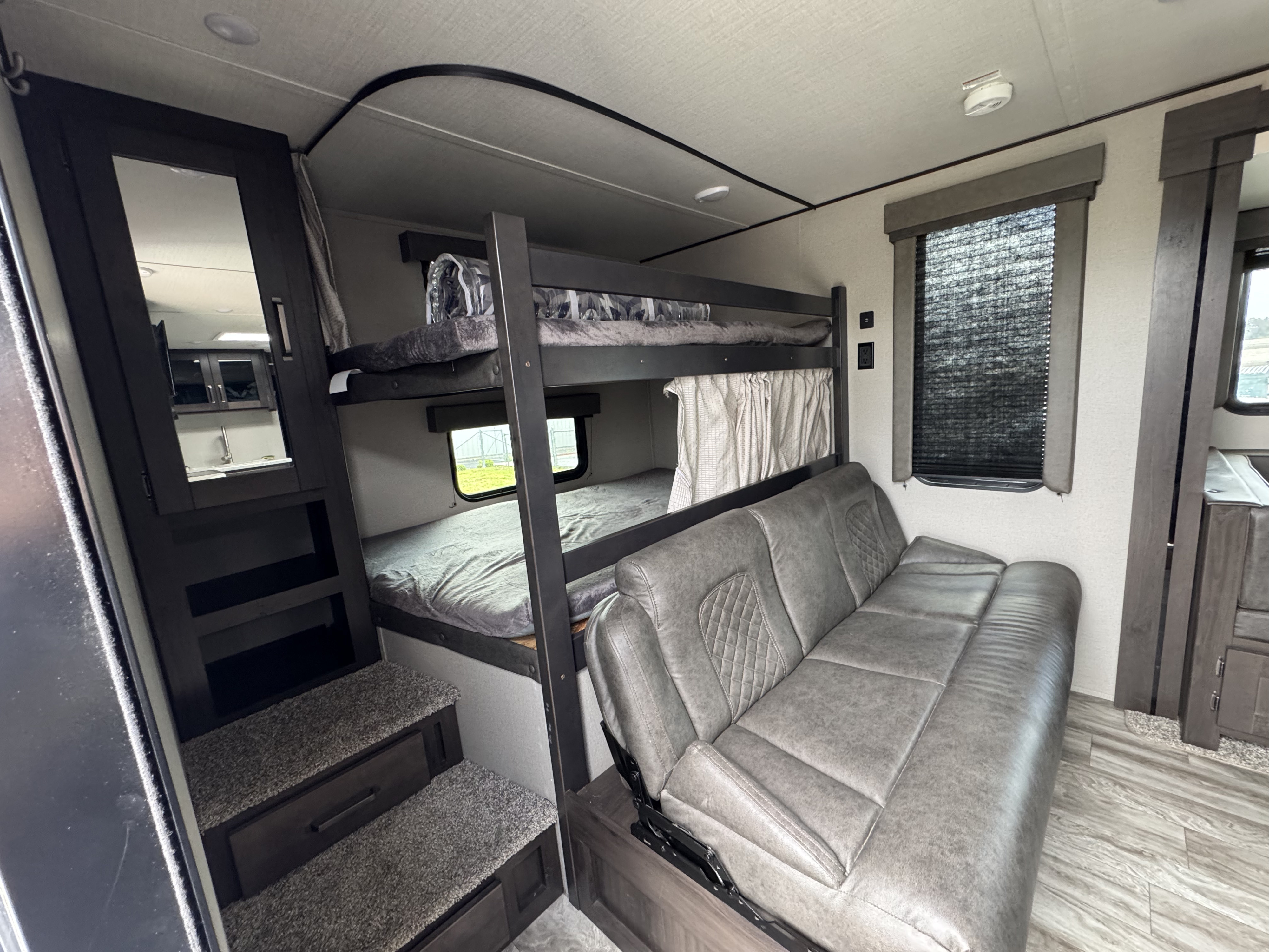 Inside an RV rental: cozy bunk beds, a versatile convertible sofa, and a compact kitchen area reflected in the mirror.. Grand Design Transcend Xplor 2022