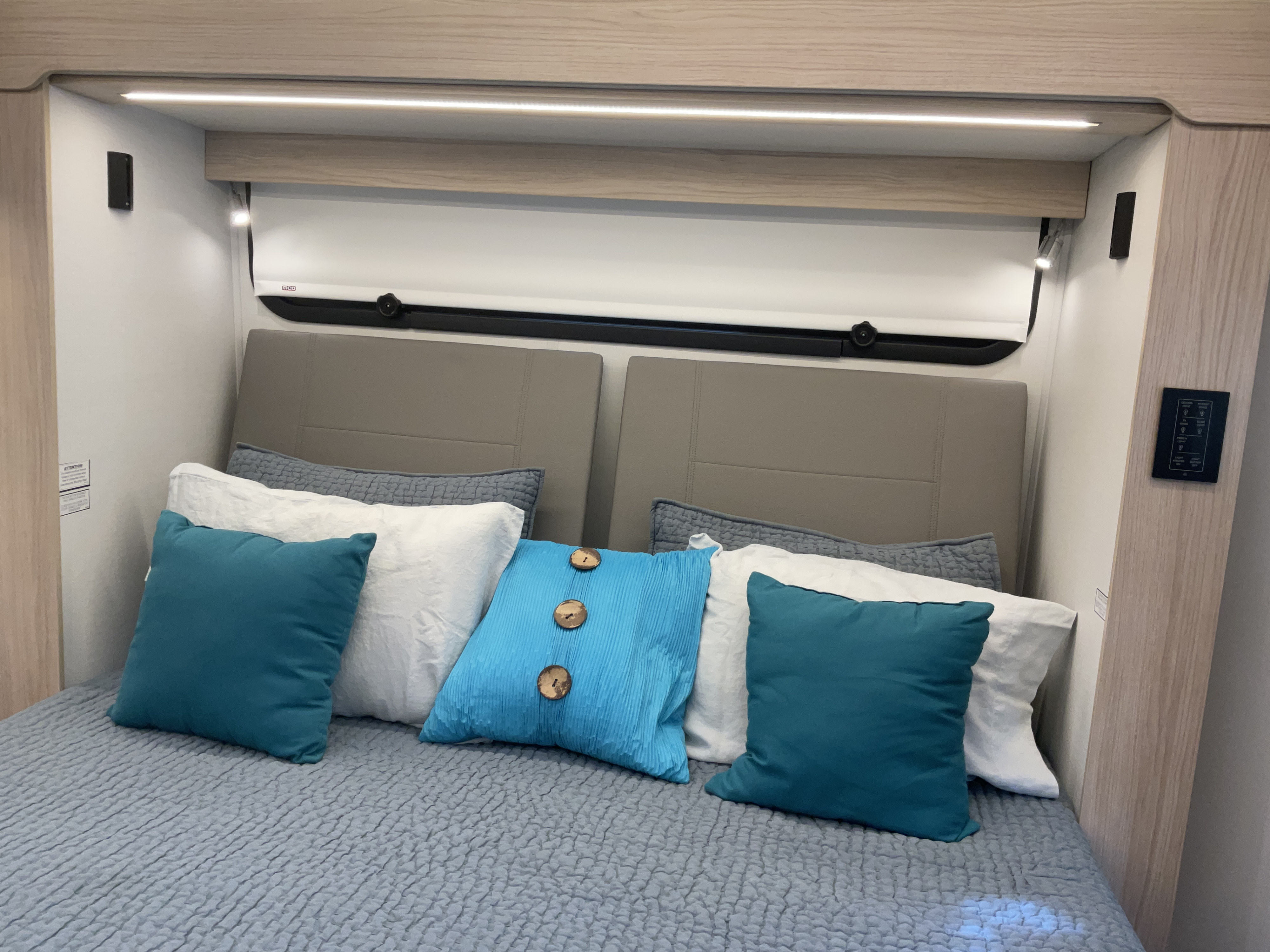Modern RV rental bedroom with textured bedding, blue pillows, and integrated lighting for a cozy journey.. Leisure Travel Vans Unity 2024