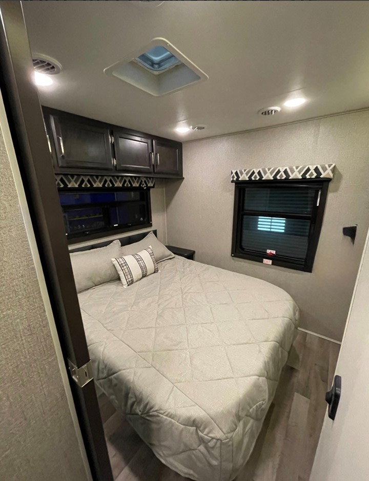 Discover this cozy rv rental bedroom: a grey bed, overhead cabinets, a skylight, and dual windows provide comfort.. Entegra Coach Odyssey 2021