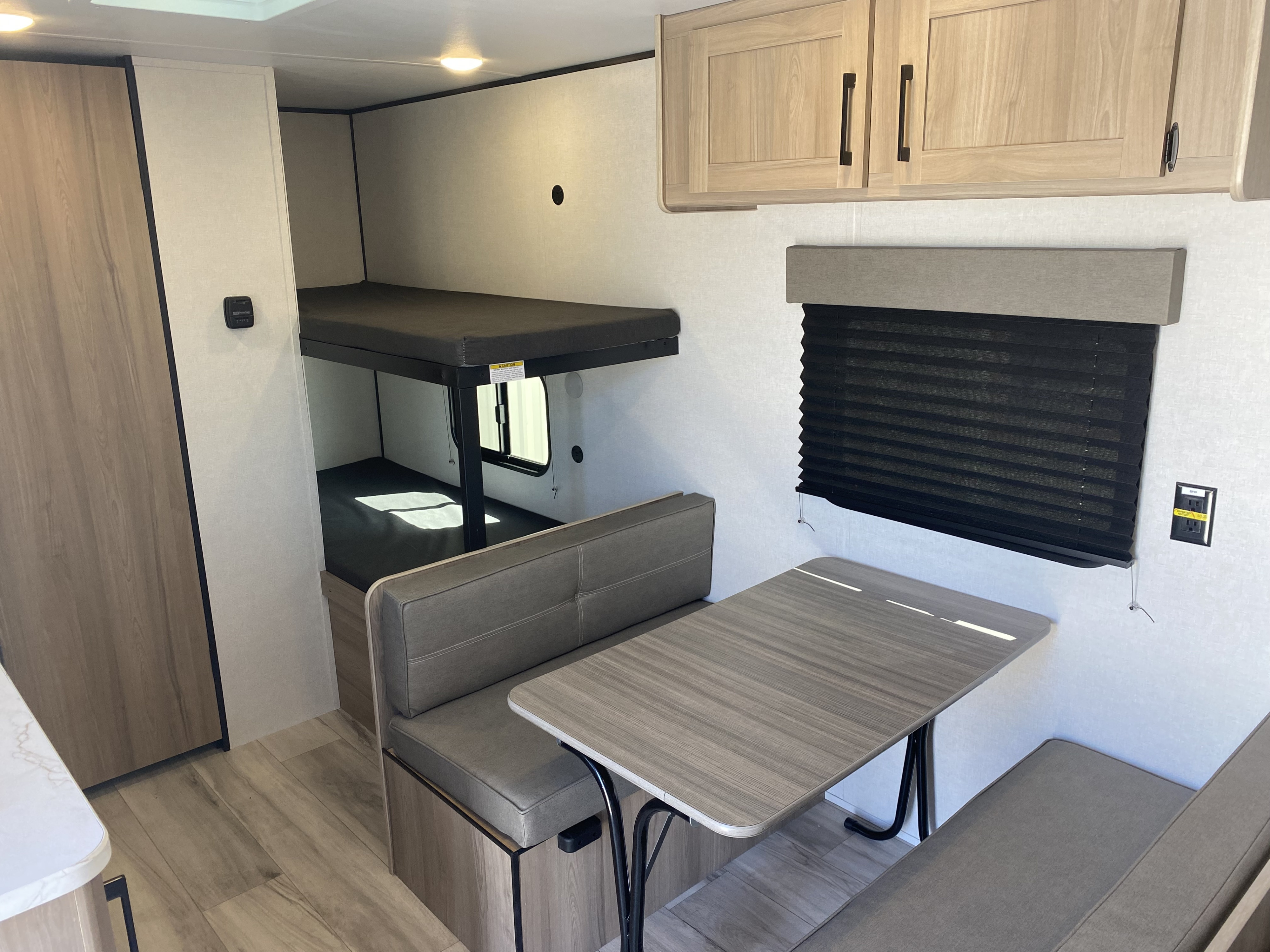 Bright RV rental interior showcasing comfortable bunk beds, a dinette, and overhead cabinets with wood-look flooring.. Keystone Coleman 2025