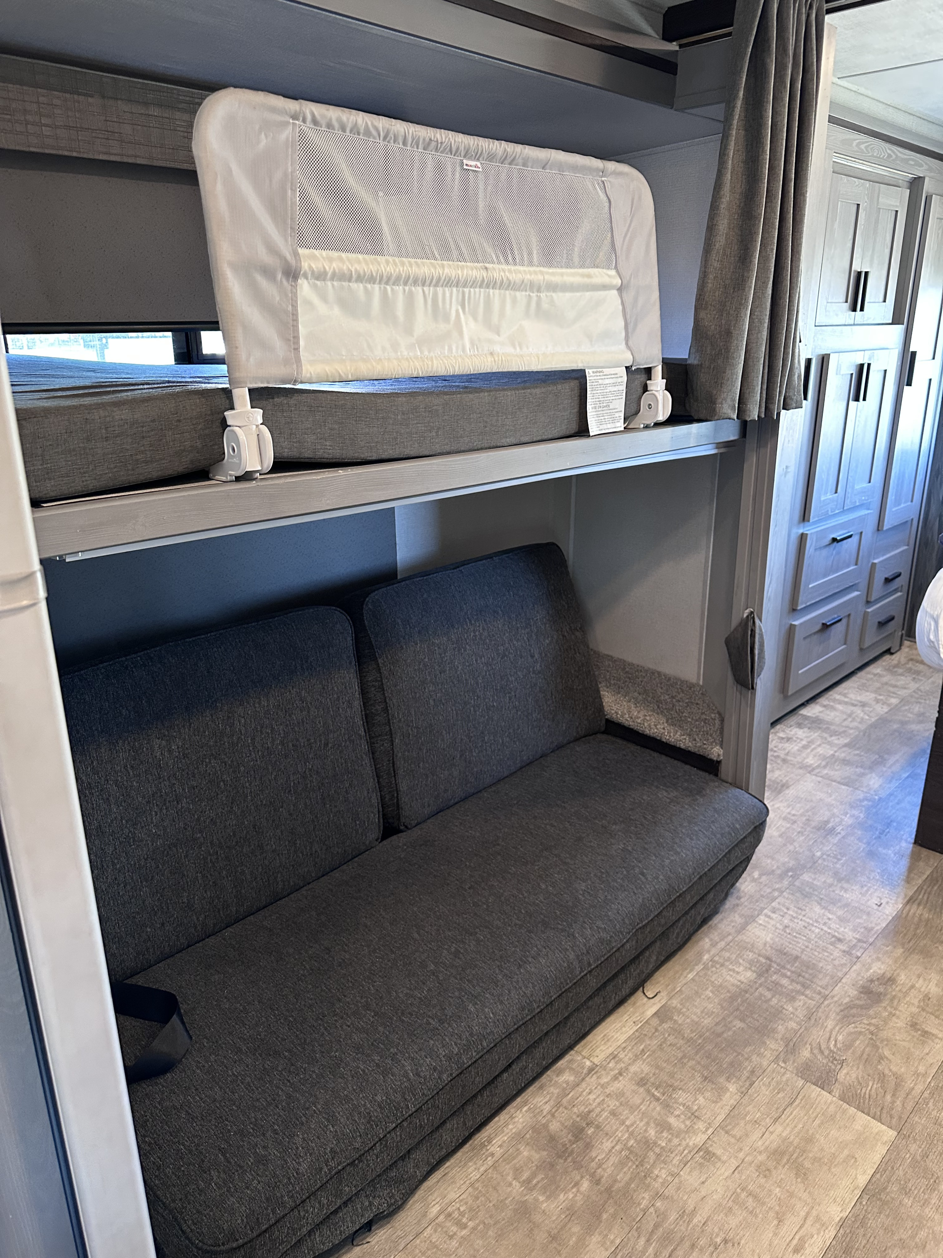 RV rental interior featuring a bunk bed with child safety rail, a dark gray sofa, and light wood cabinets, ideal for family trips.. Forest River Solera 32DSB 2022