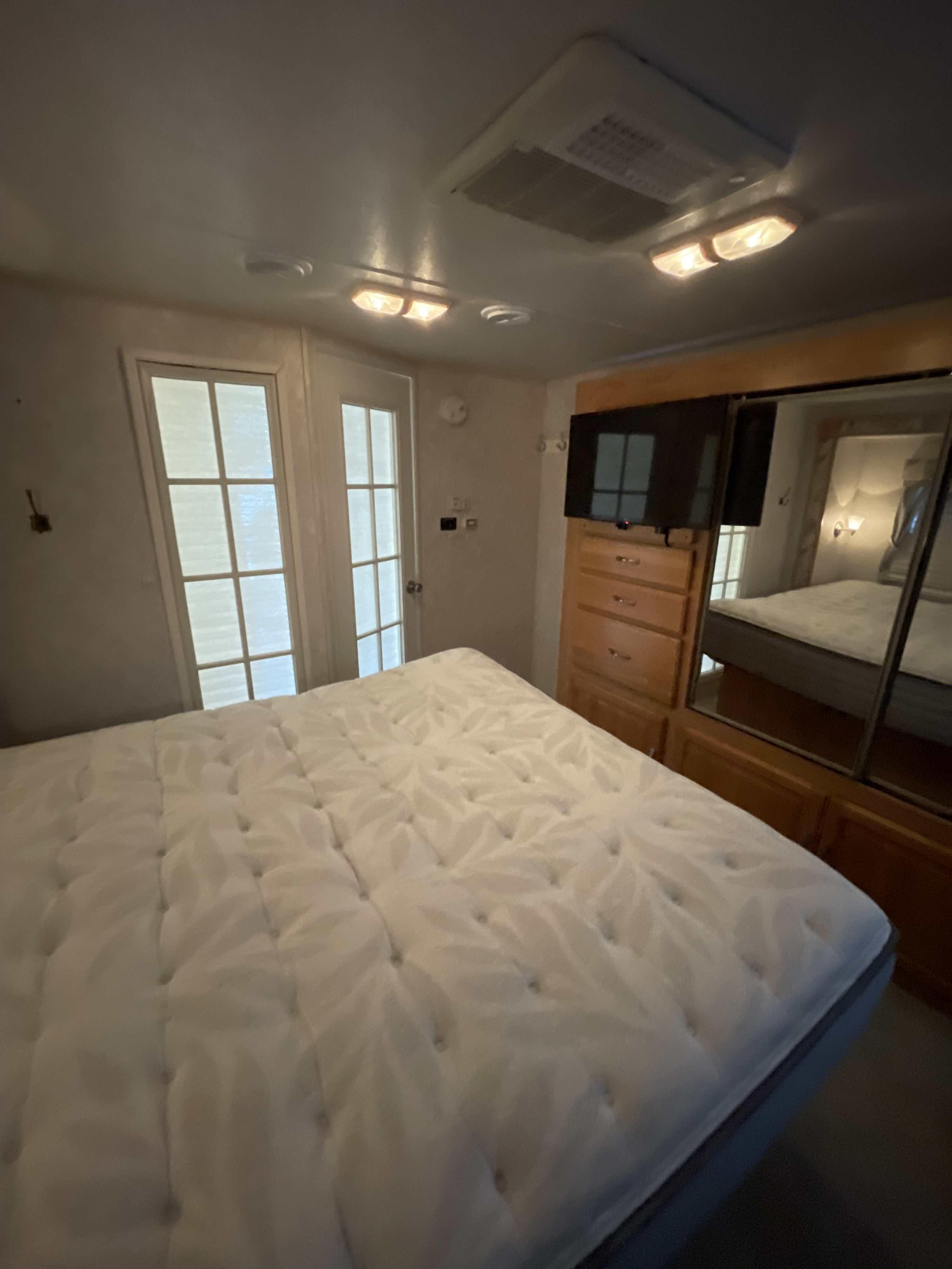 Interior of an RV rental bedroom featuring a large bed, wall-mounted TV, mirrored closet, and two glass-paned doors.. R-Vision Condor 2004
