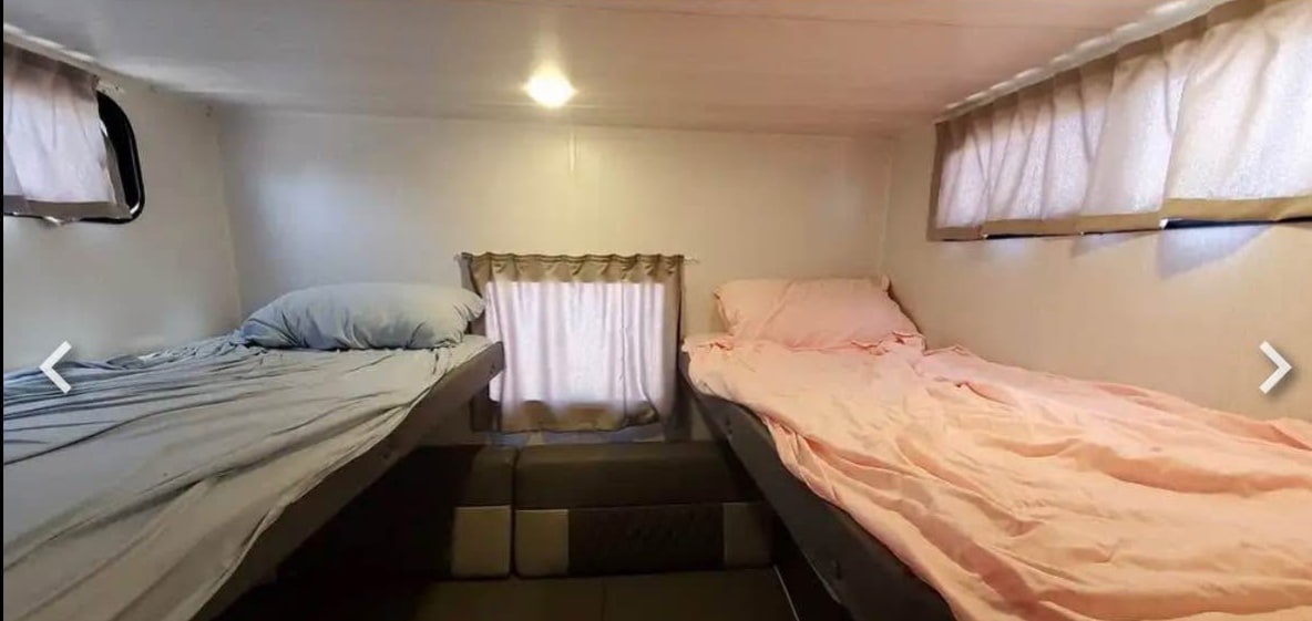 Compact RV rental sleeping area with two side-by-side beds (blue & pink sheets) and windows.. Forest River Cruise Lite 2022