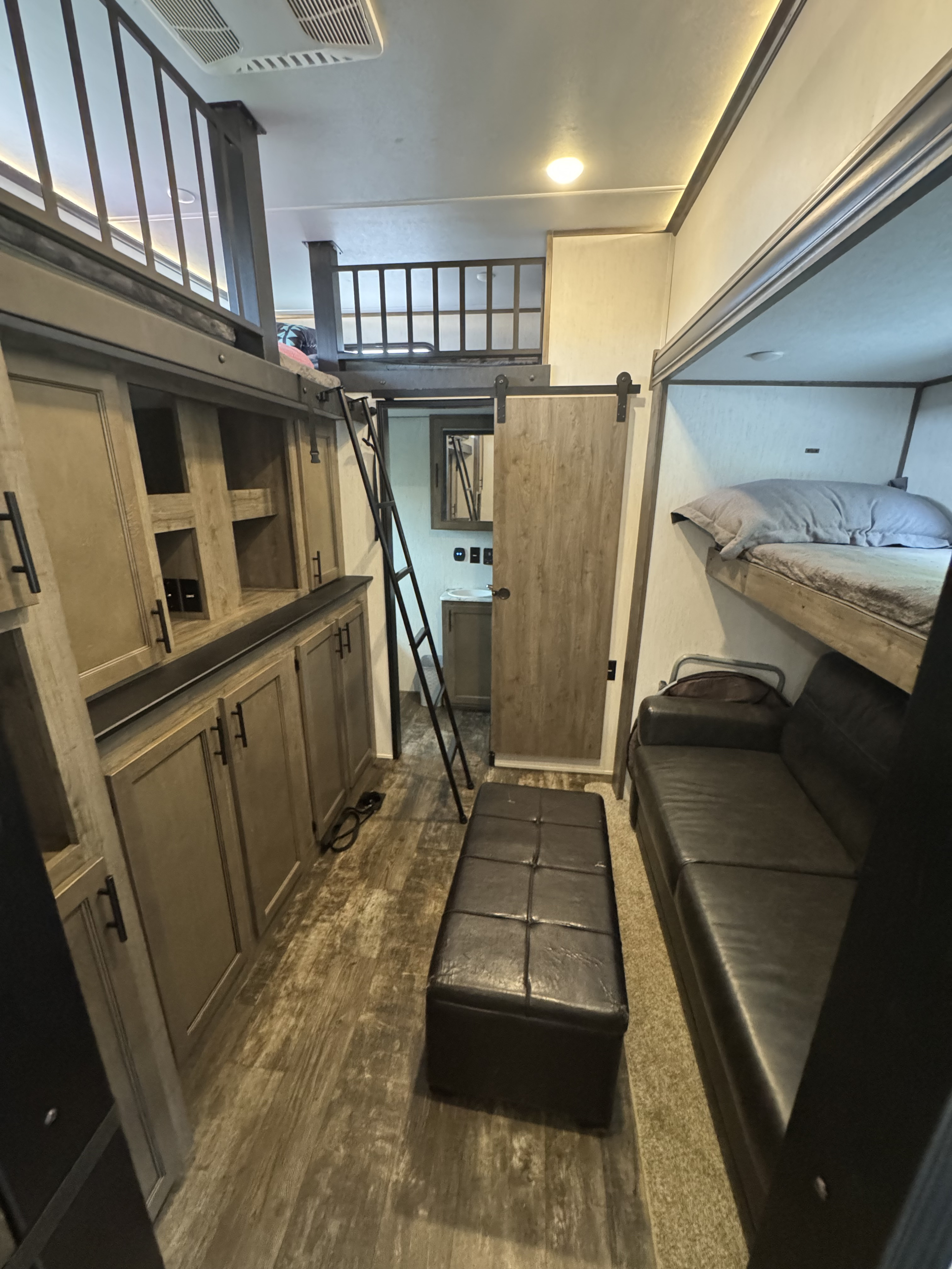 Cozy RV rental interior showcasing bunk beds, a loft, living area with sofa, and sliding barn door to the bathroom.. Forest River Sabre 2021
