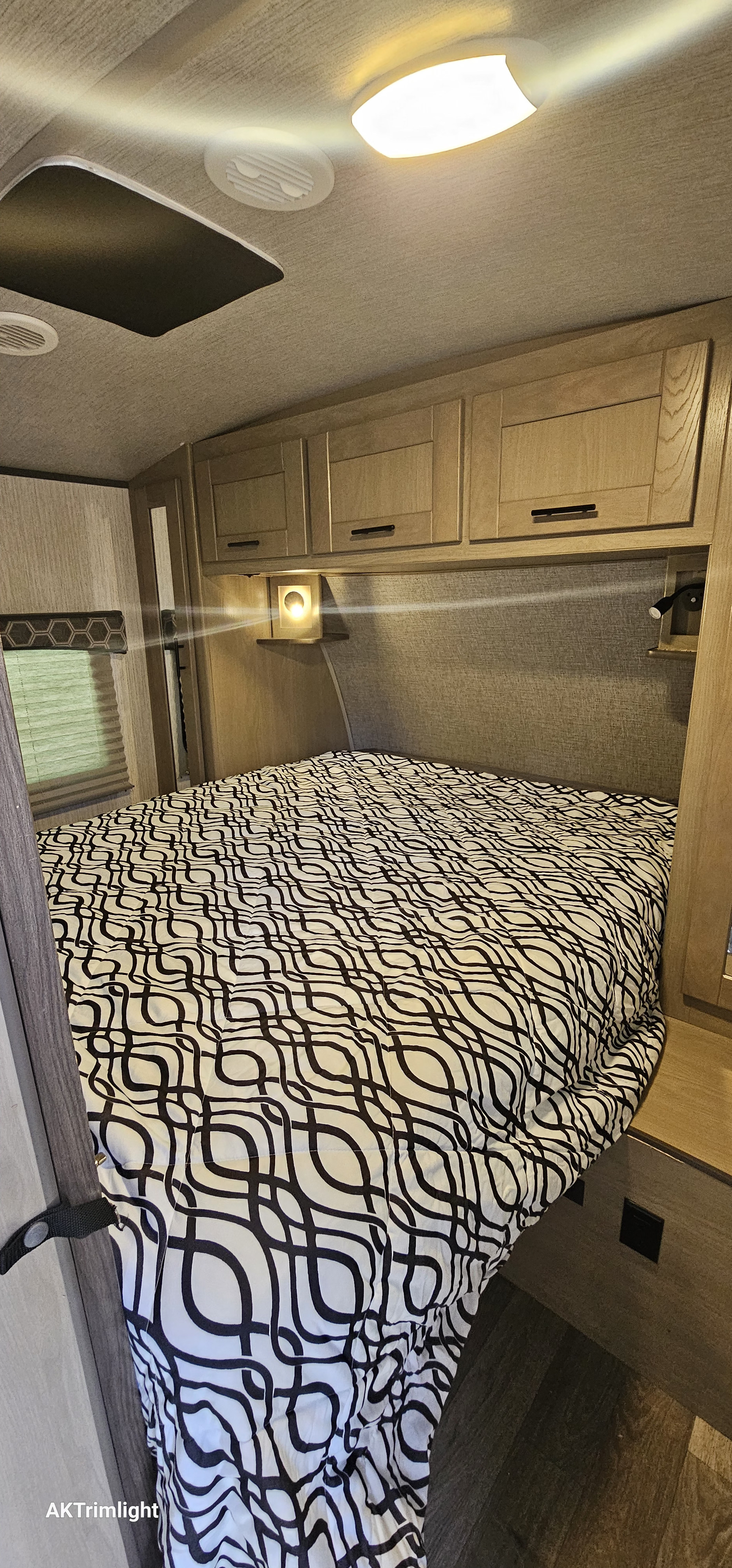 Bright and cozy RV rental bedroom: patterned bed, overhead storage, and illuminated reading lights.. Heartland RVs Sundance Ultra Lite 2021