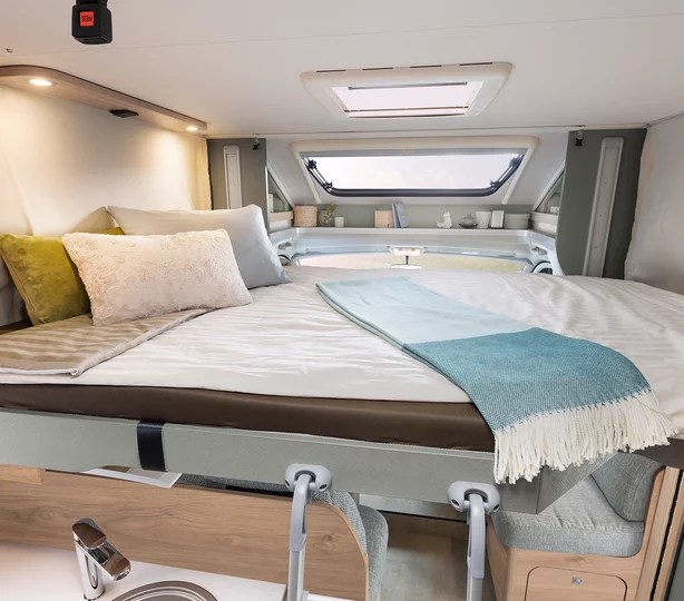Cozy RV rental interior shows a comfortable sleeping area with pillows, a blanket, and an overhead window. Perfect for travel.. Dethleffs Juyst T 7052 2023