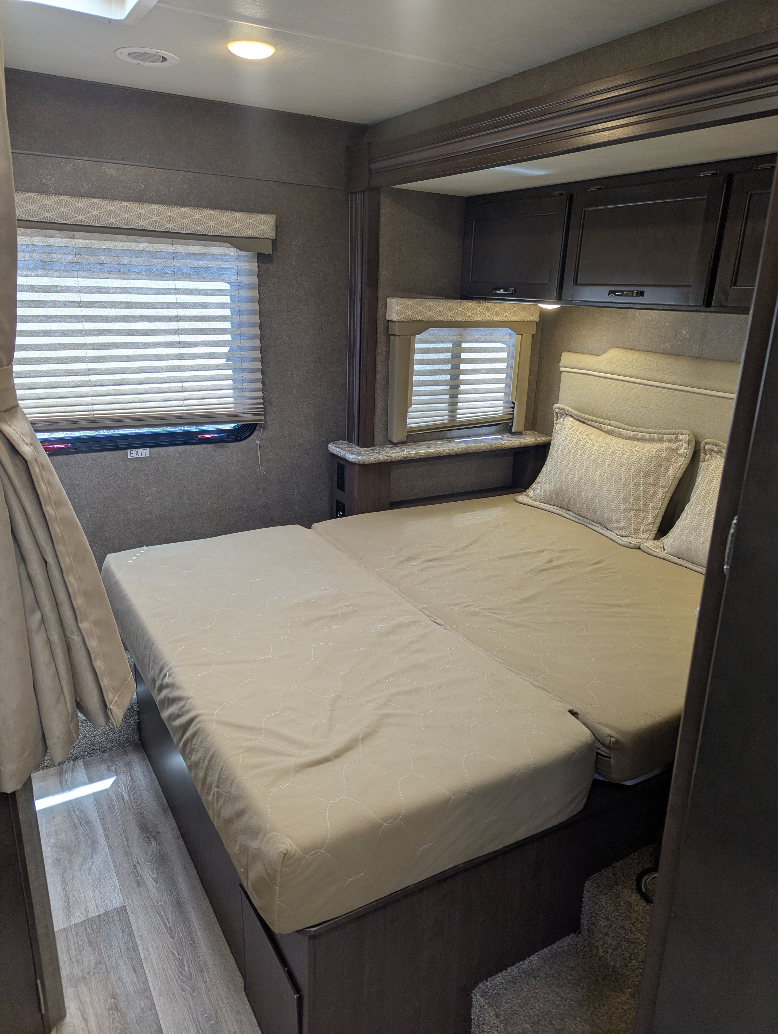 RV rental bedroom with a large, convertible bed, two windows with blinds, dark overhead storage cabinets, and ambient lighting.. Thor Motor Coach Freedom Elite 2020
