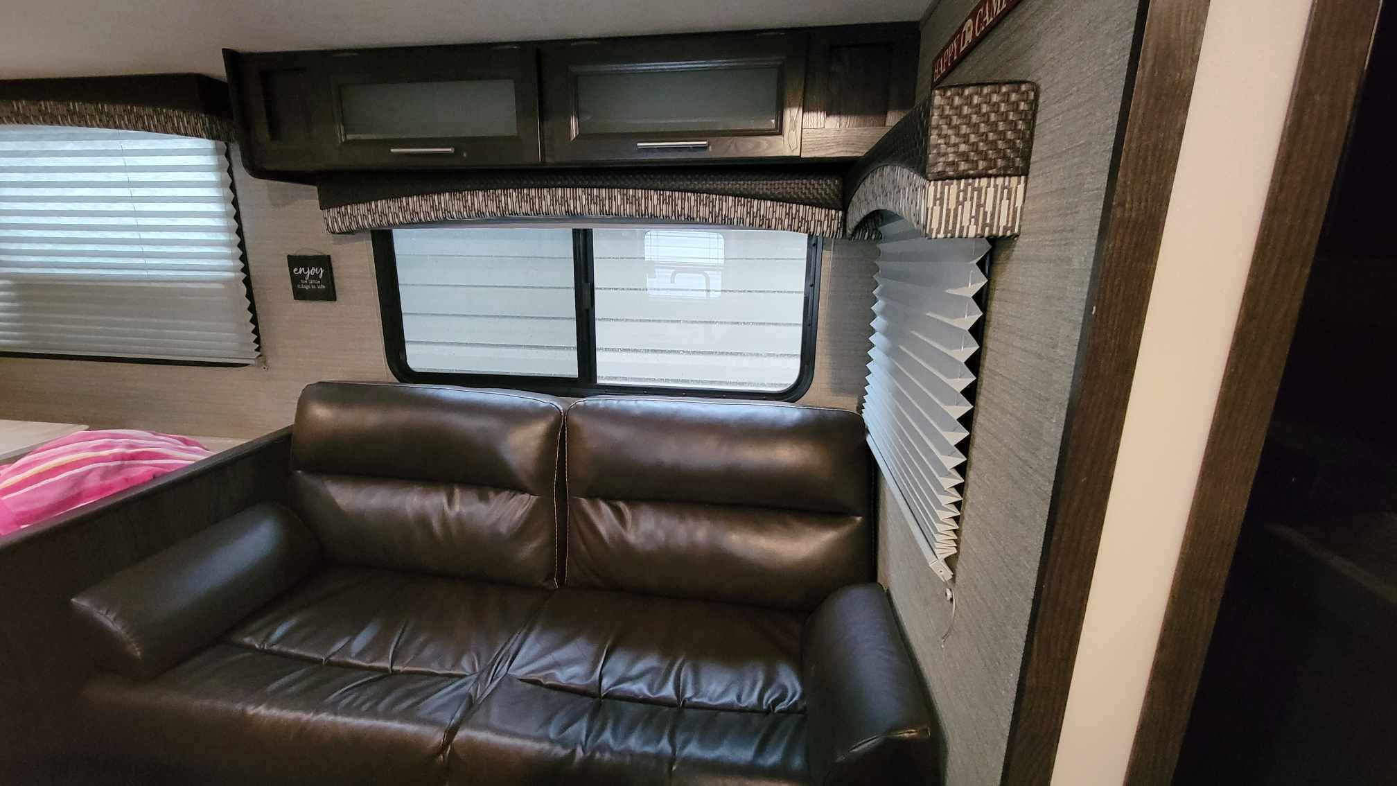 Inside this rv rental: A dark sofa, overhead cabinets, and window blinds. A compact and comfortable RV living area.. Dutchmen Kodiak Express 2018