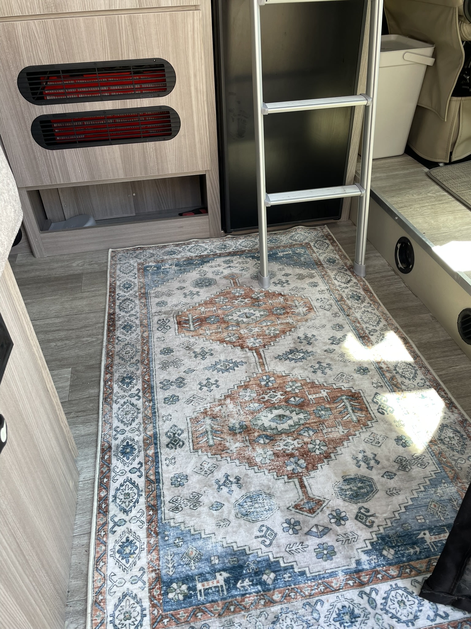 Cozy RV rental interior featuring a patterned rug, an access ladder, and wood-look cabinetry with vents.. Thor Scope 2024