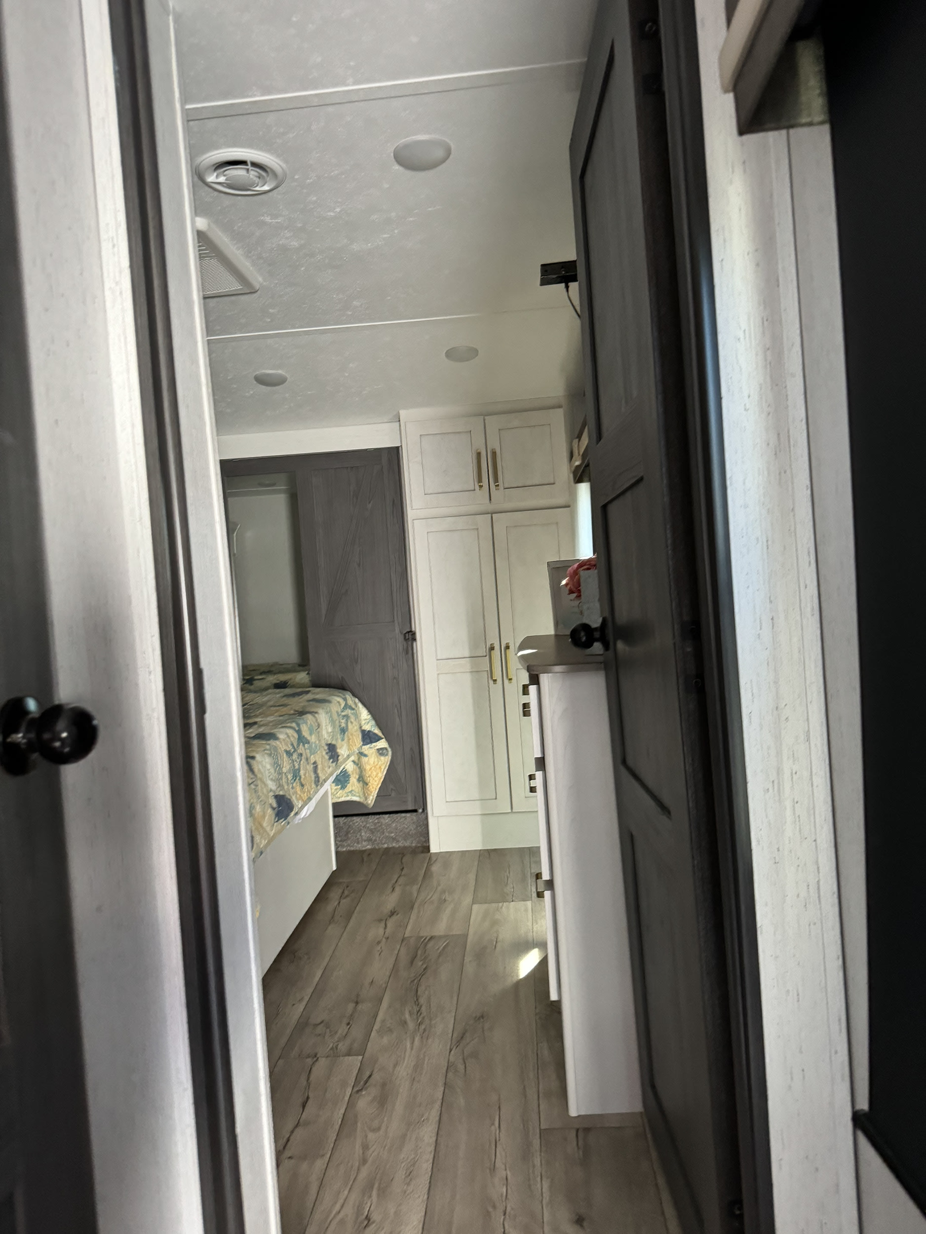 Modern RV rental interior: bedroom view with wood floors, white cabinets, and patterned quilt.. Astoria Platinum 2022