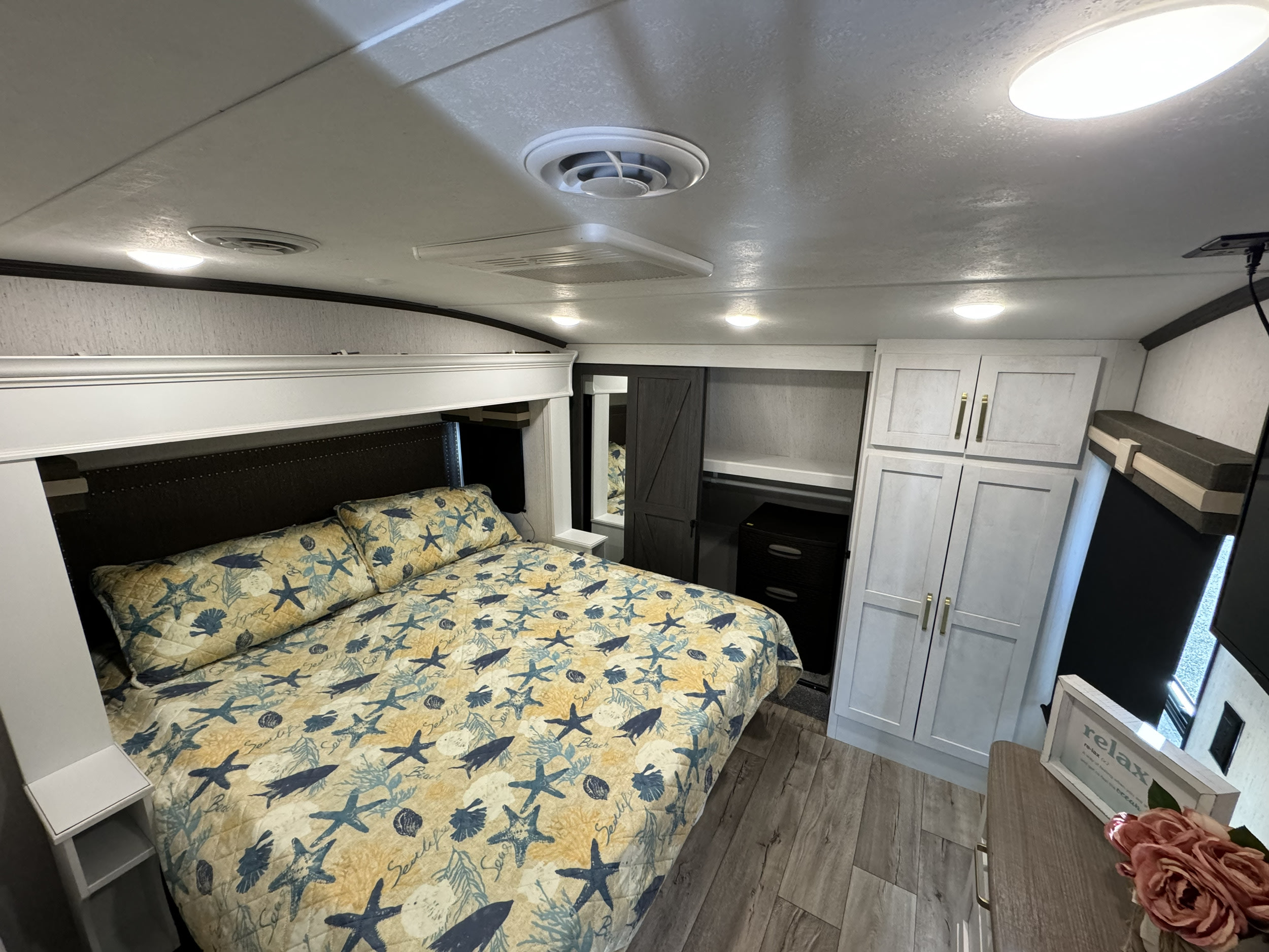 Cozy RV rental bedroom featuring a nautical-themed bed, overhead storage, and stylish barn door closet.. Astoria Platinum 2022
