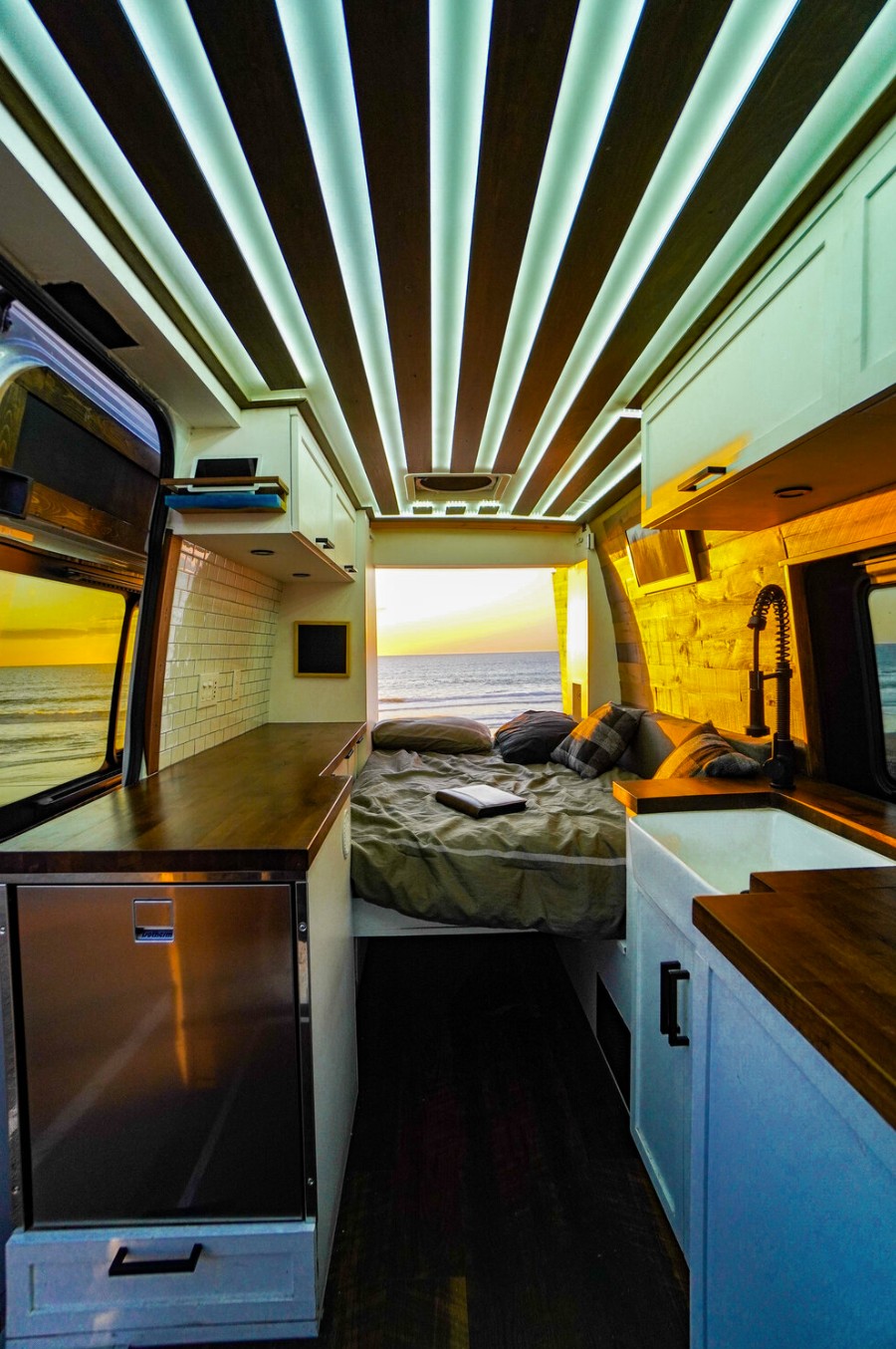 Stunning rv rental interior: modern van with ocean sunset view, bed, kitchen, and ambient ceiling lights for ultimate travel.. Mercedes-Benz Sprinter 2019