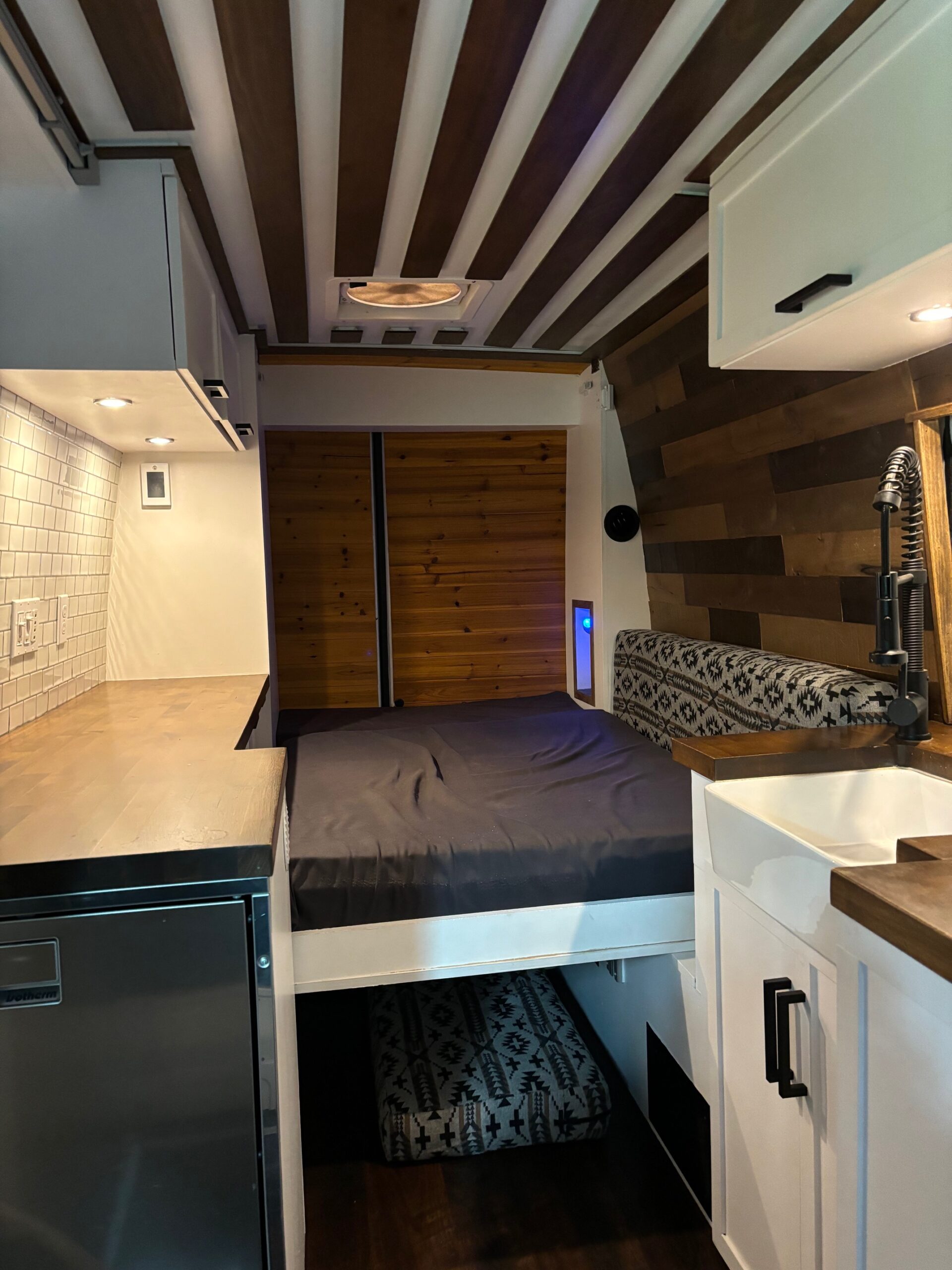 Modern RV rental interior: compact kitchen with sink, comfy bed, wood ceiling, and stylish storage solutions for your adventure.. Mercedes-Benz Sprinter 2019