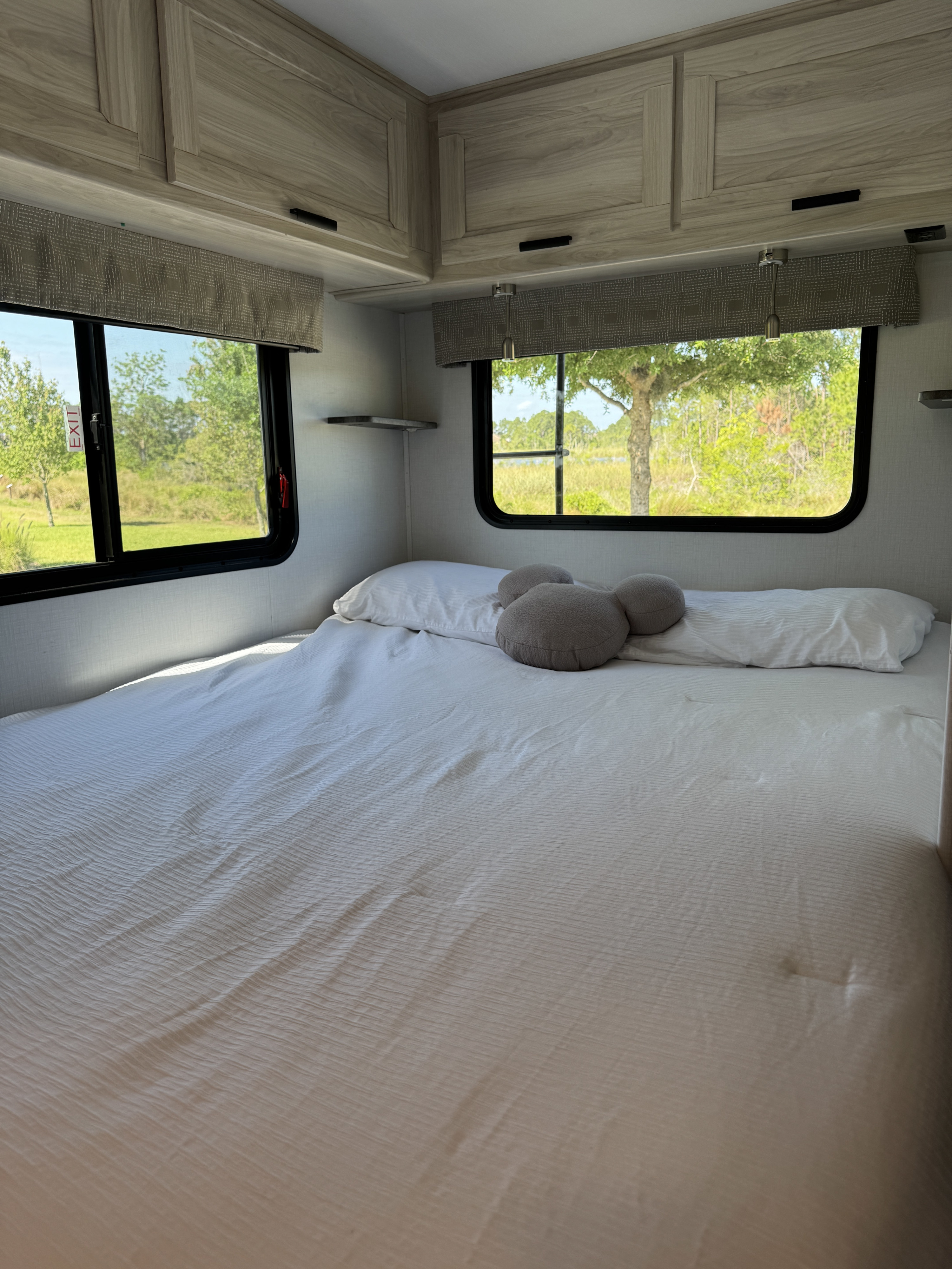Spacious RV rental bedroom with a large bed, crisp white bedding, cozy pillows, and scenic windows revealing lush nature.. Forest River Sunseeker LE 2024