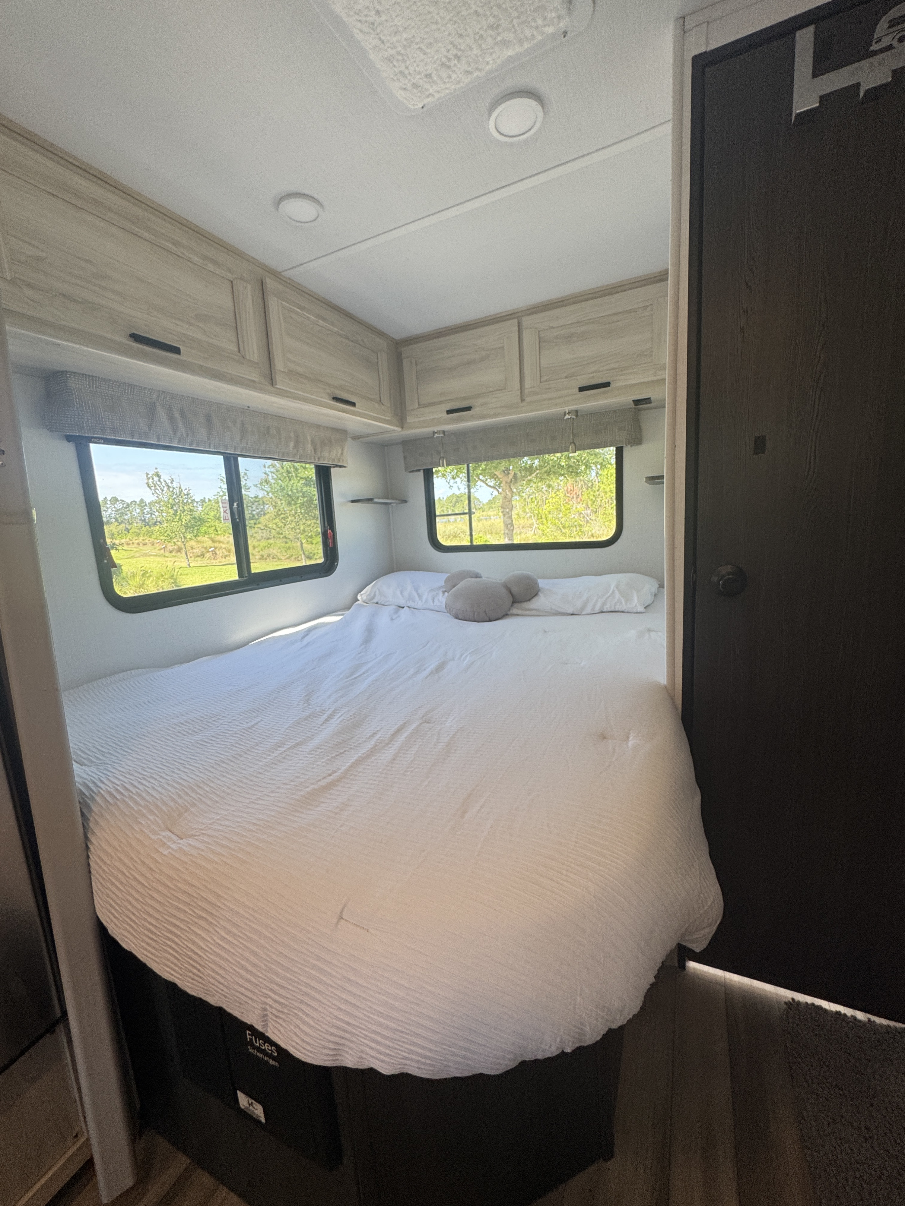 Cozy RV rental bedroom with white bed, nature views from windows, and ample overhead storage.. Forest River Sunseeker LE 2024