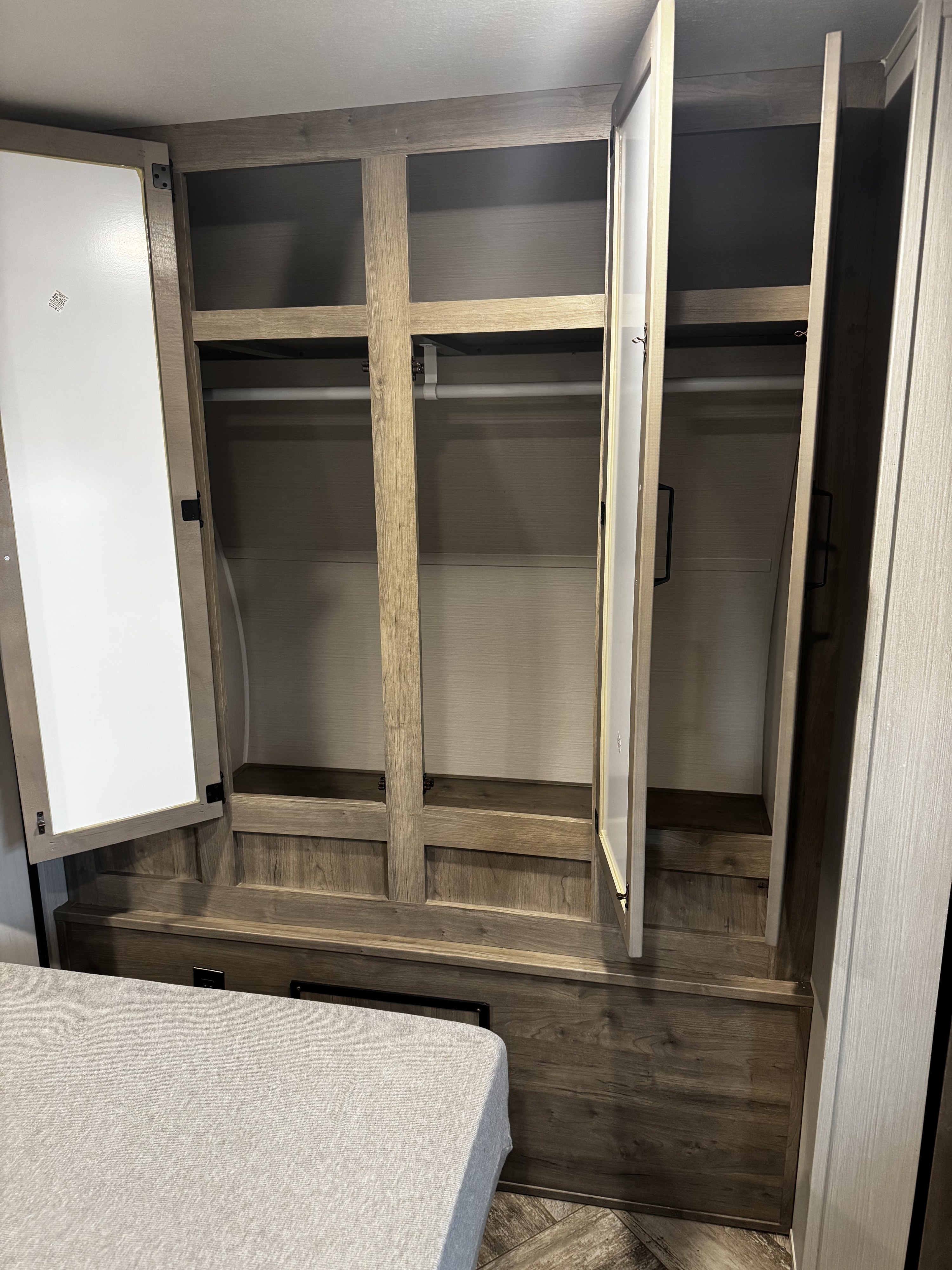 RV rental bedroom with open wood-grain wardrobe, featuring hanging rods & shelves. A bed is in the foreground.. Forest River Puma 2026