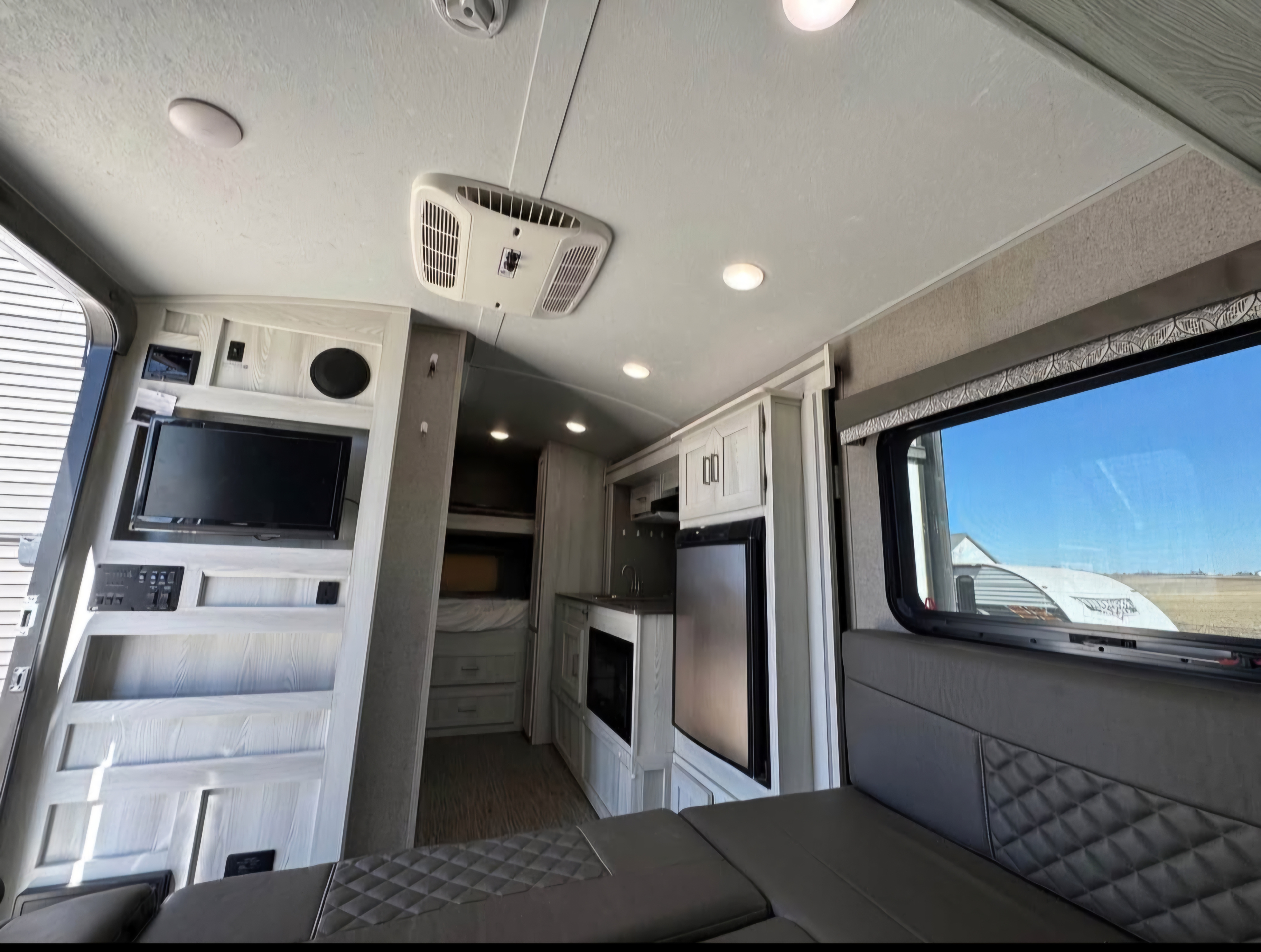 Modern RV rental interior: view of living area with padded seating, TV, kitchenette with fridge, and bunk beds. Bright and functional.. Forest River Rockwood Geo Pro 2019