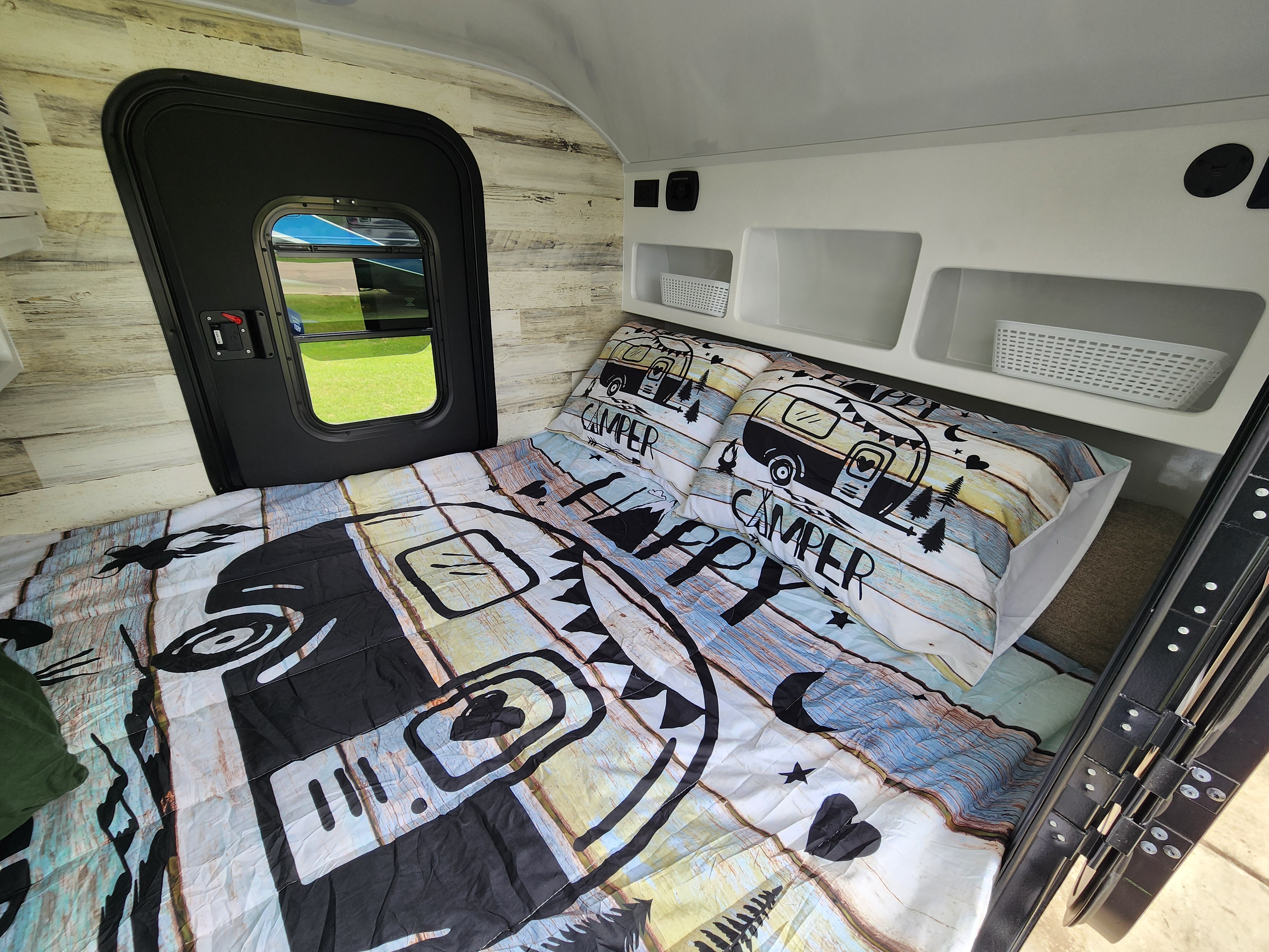 Cozy RV rental interior with a "Happy Camper" bed, storage cubbies, and a side door.. Modern Buggy Lil Buggy 10RK 2025