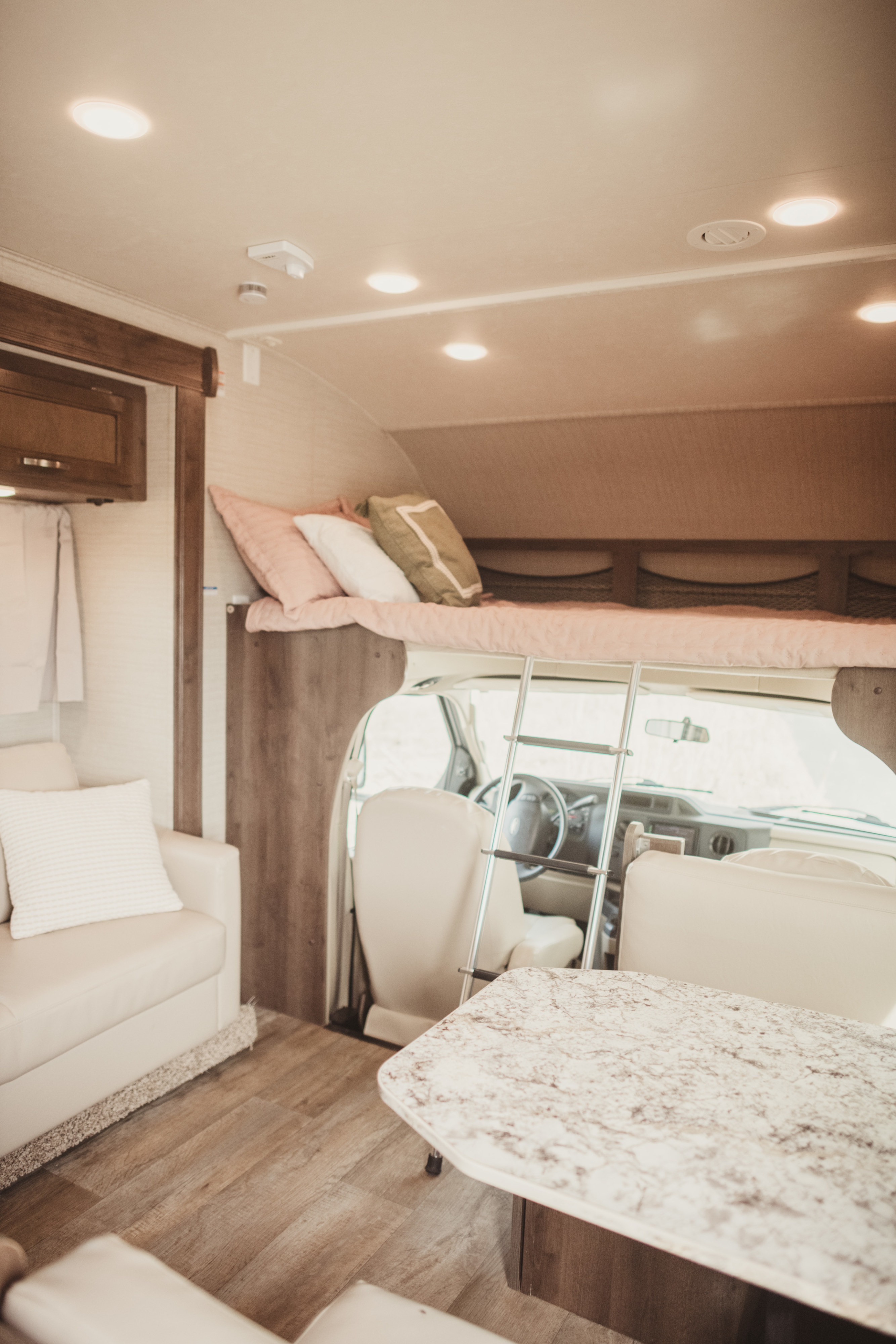 Bright RV rental interior: cab-over bed with ladder, sofa, dining table, and wood flooring.. Jayco Redhawk 2019