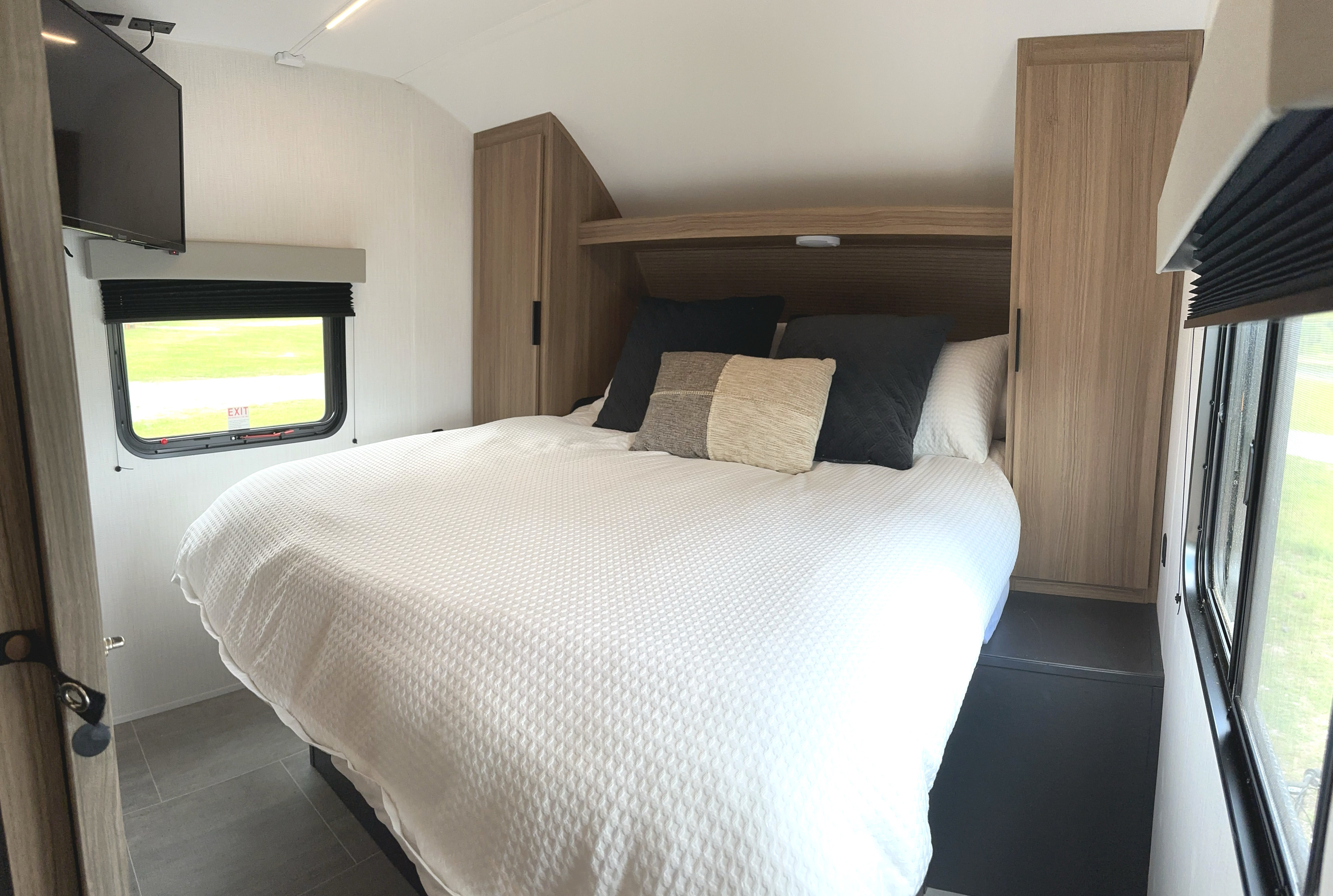 Inviting RV rental bedroom featuring a comfortable bed, integrated storage, wall-mounted TV, and window.. Heartland Trail Runner 2025