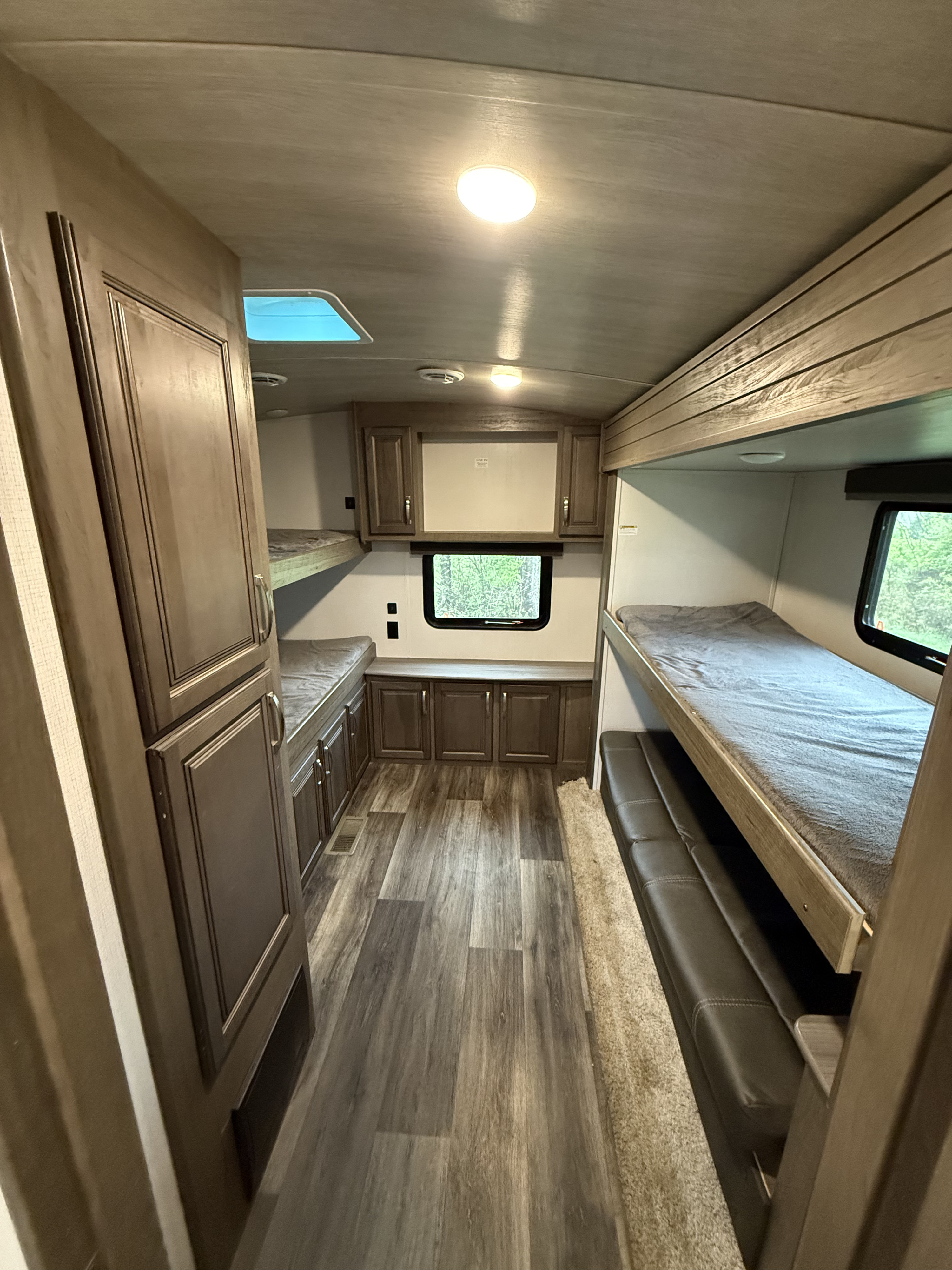 RV rental interior showcasing a bunkhouse with two sets of beds, wood-look flooring, central cabinetry, and seating.. Keystone RV Cougar 2022