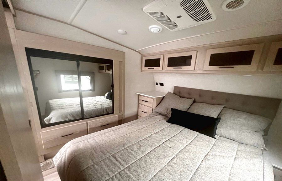 Inside an RV rental: a cozy bedroom features a bed, mirrored closet, overhead storage, and AC units.. Forest River Flagstaff Super Lite 2023