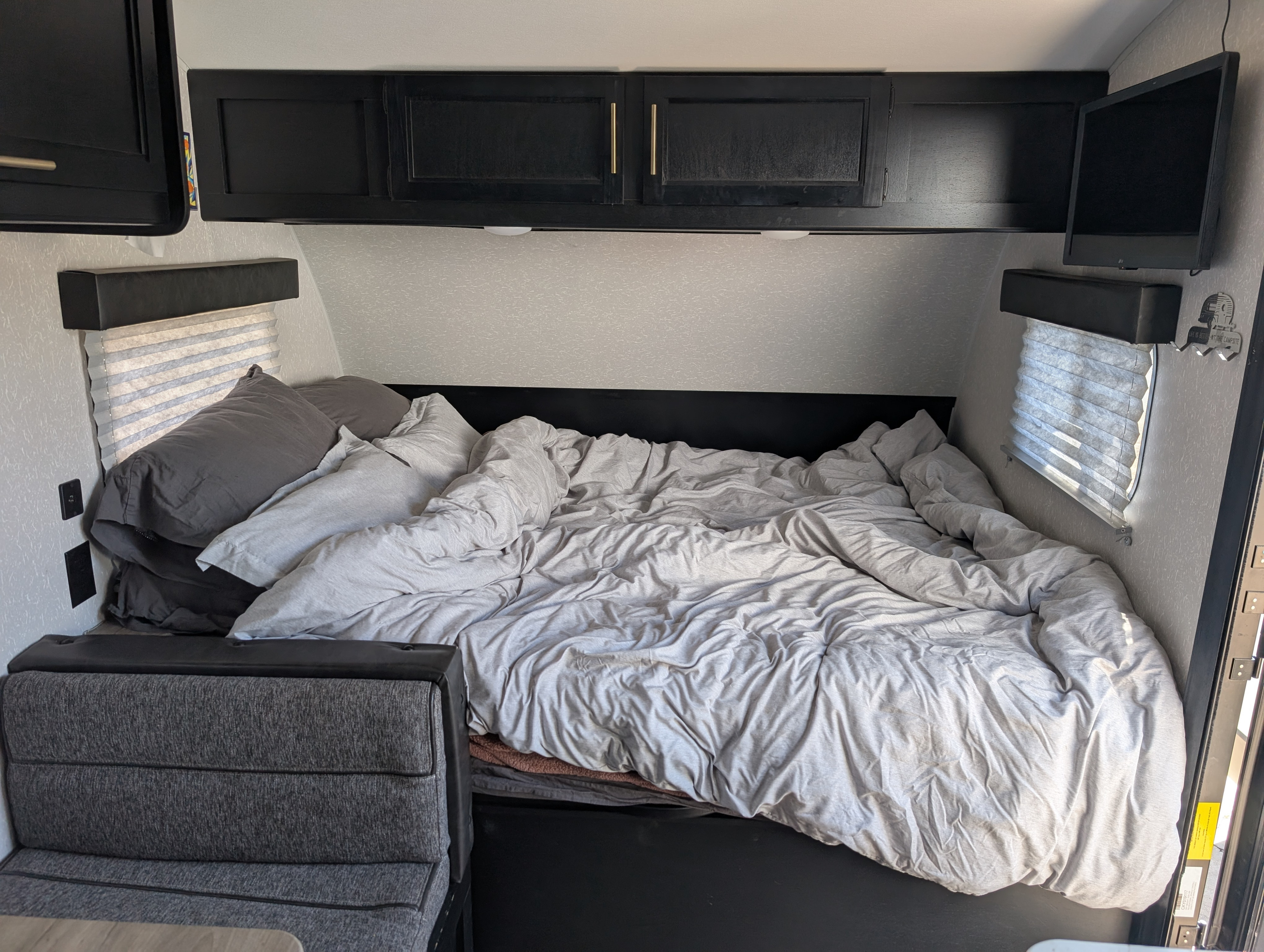 Compact RV rental bedroom featuring a comfy bed with grey linens, dark cabinets, and a small TV.. Forest River Cherokee Wolf Pup 2022