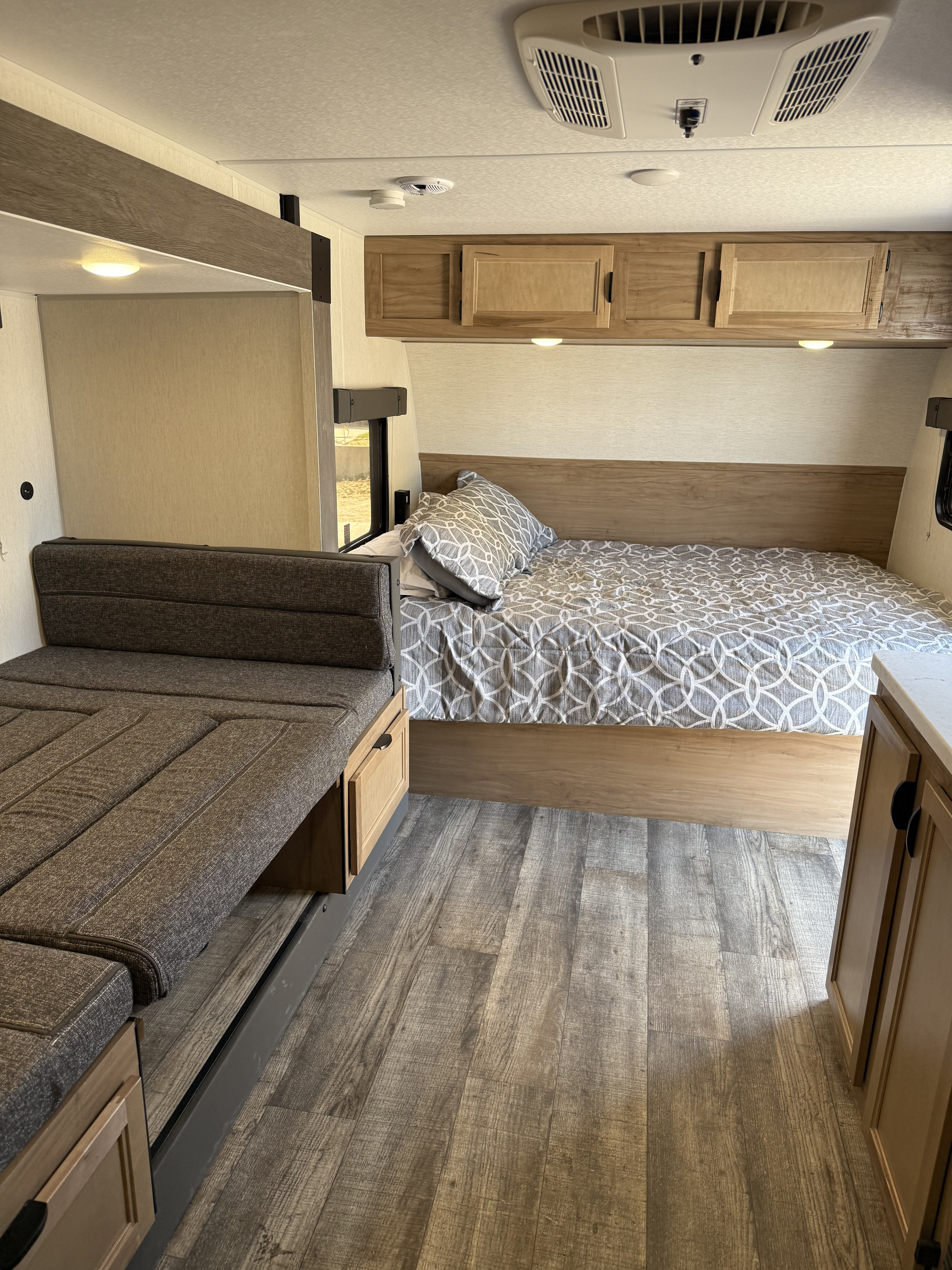Comfortable rv rental interior featuring a bed with patterned duvet, sofa, wood-look floor, and overhead AC unit.. Forest River Wolf Pup Limited 2024