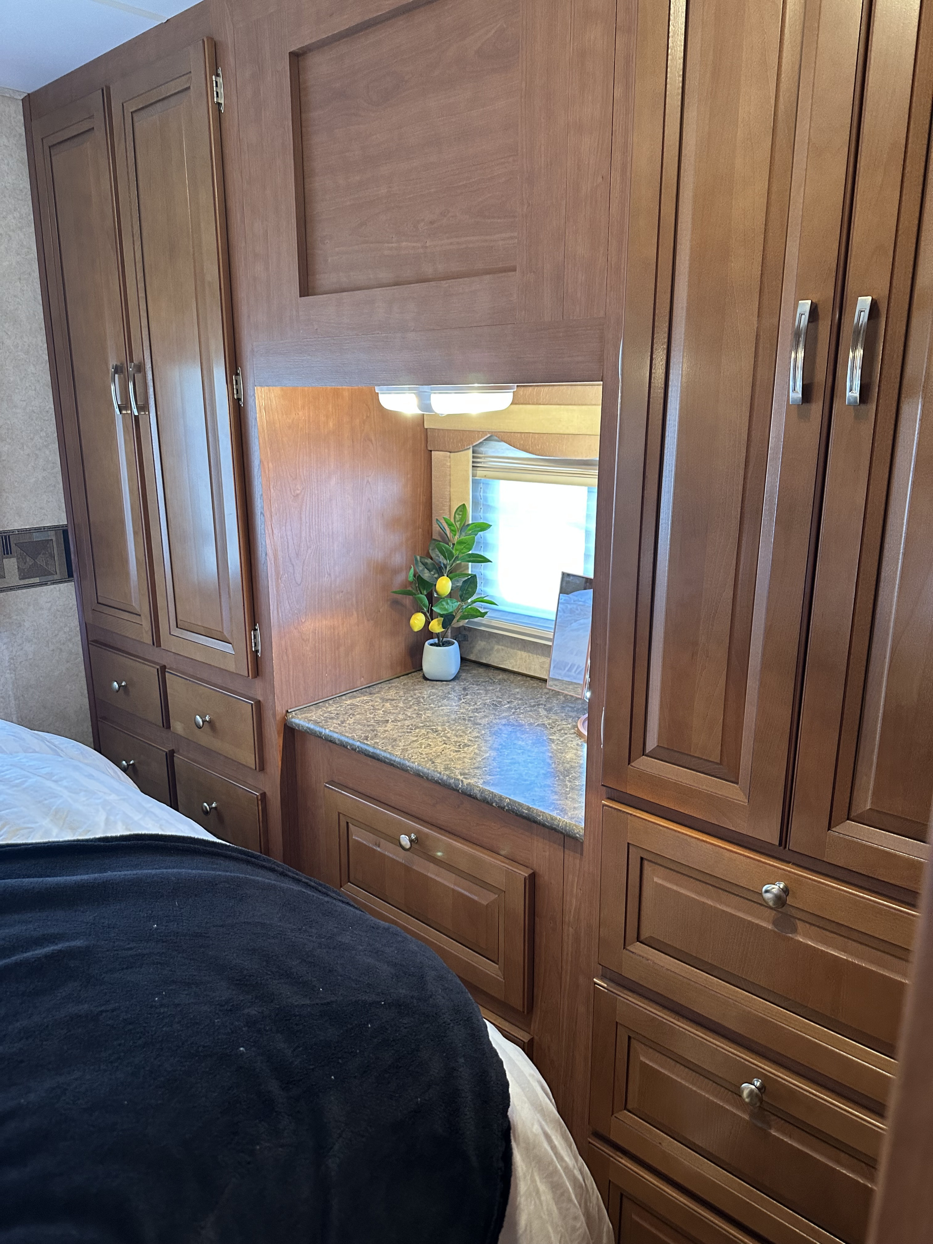 This RV rental bedroom features cozy built-in storage with wood cabinets, drawers, and a small vanity area by the window.. Forest River Georgetown 2011