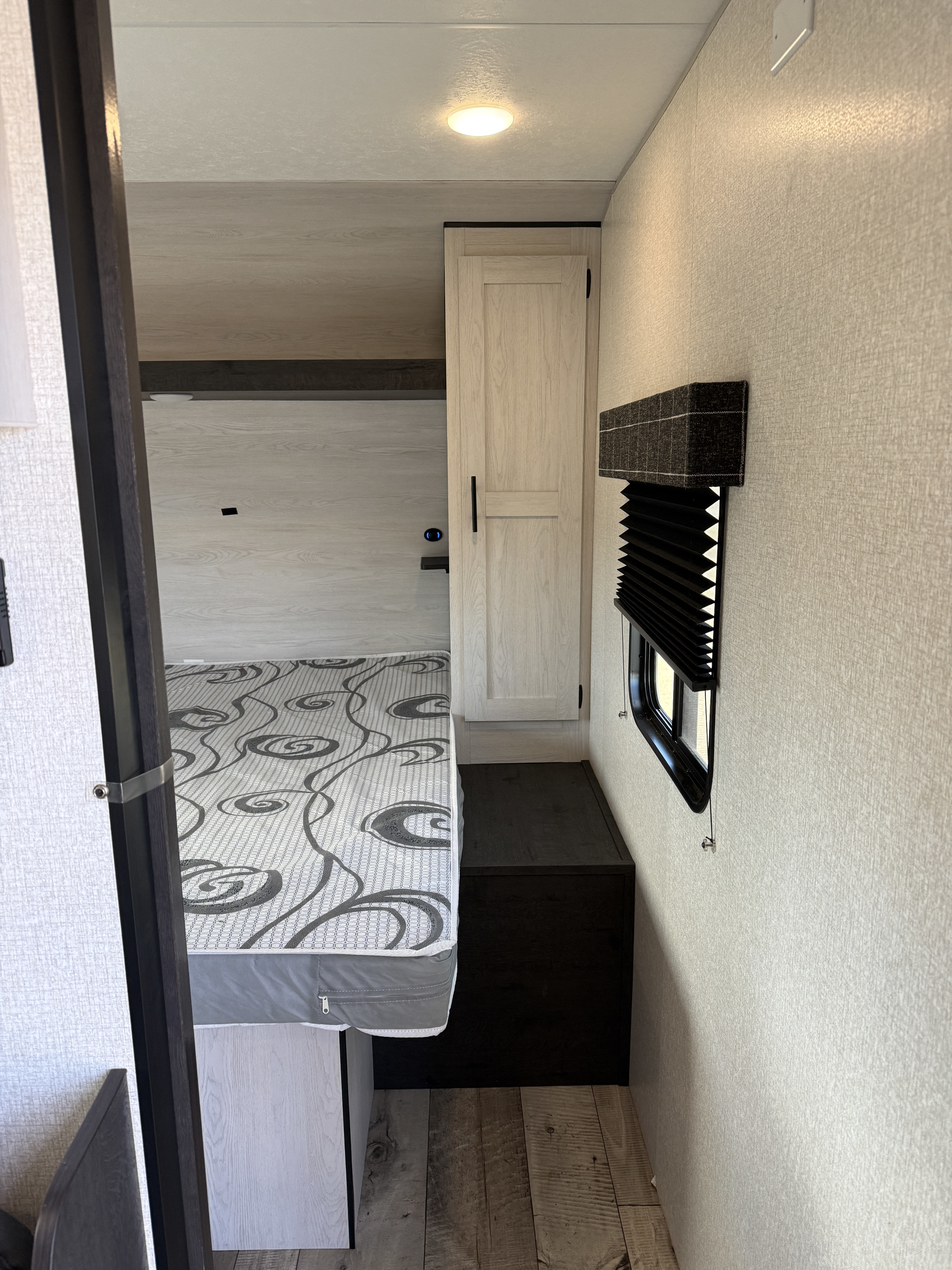 Cozy RV rental bedroom with patterned bed, light wood floor, small window, & cabinet storage.. Sportsmen SE 2022