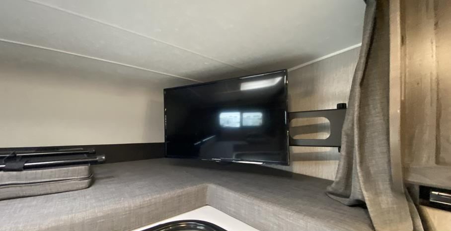 This RV rental shows an interior with a TV mounted on a wall above a cushioned bench, and a curtain on the right.. FORD Coachhmen Lepre260QB 2023