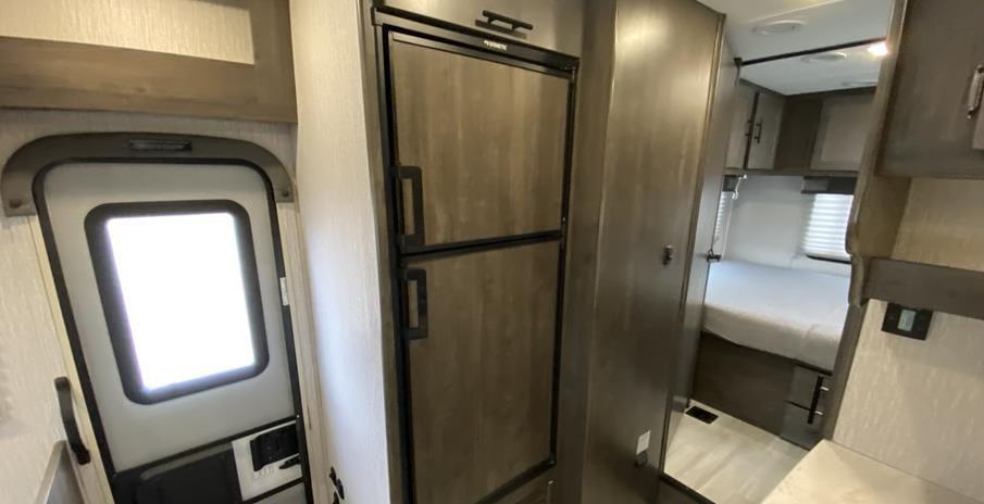 Inside an RV rental, showing the main entry door, a compact refrigerator, and a cozy bed area. Ideal for travel.. FORD Coachhmen Lepre260QB 2023