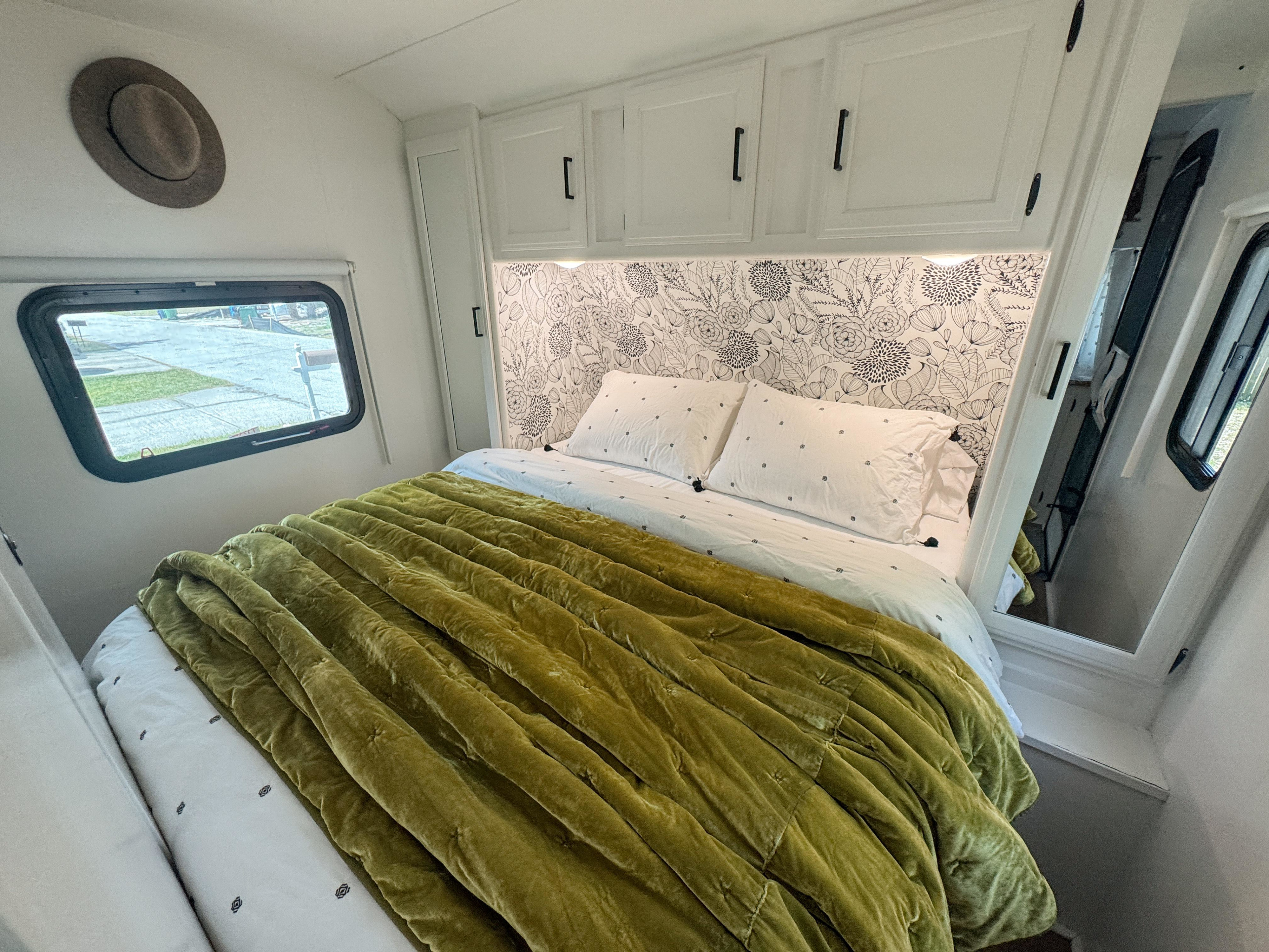 Cozy RV rental bedroom featuring black and white floral wallpaper, a plush green velvet bed, and smart overhead storage.. Keystone Passport 2017