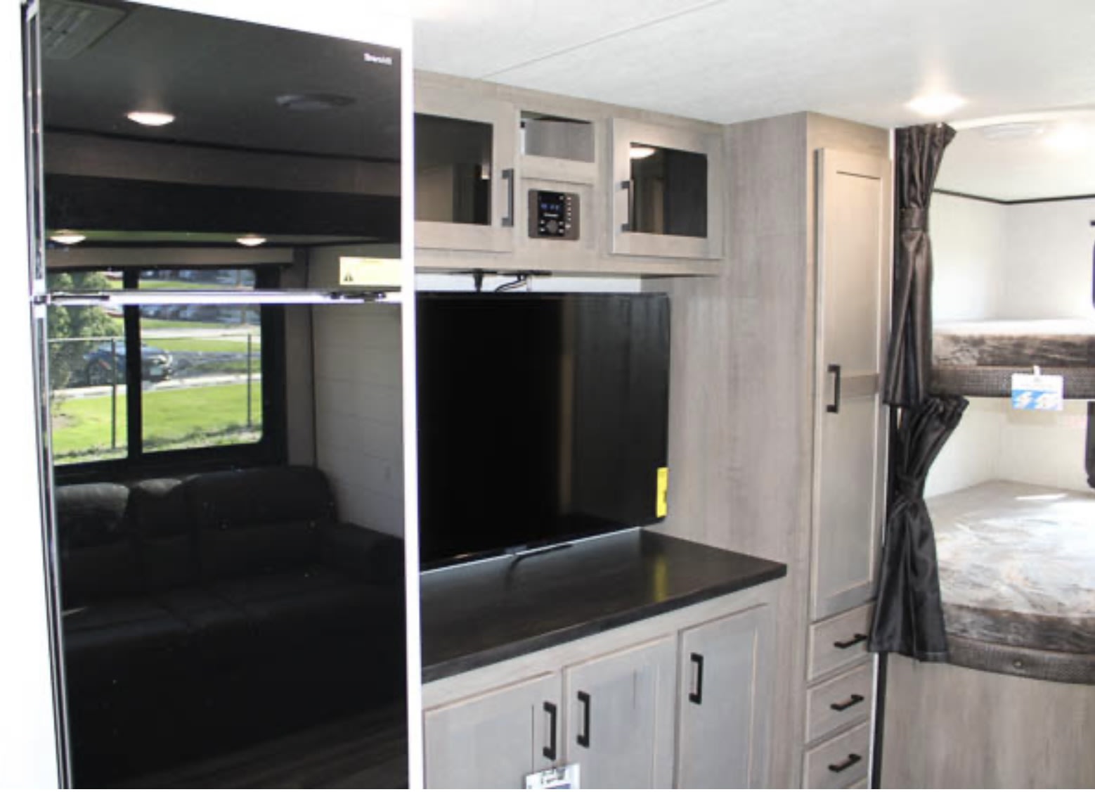 Inside an RV rental: entertainment unit, bunk beds, and storage. A reflective surface on the left shows the living area.. Jayco Jay Flight 2024
