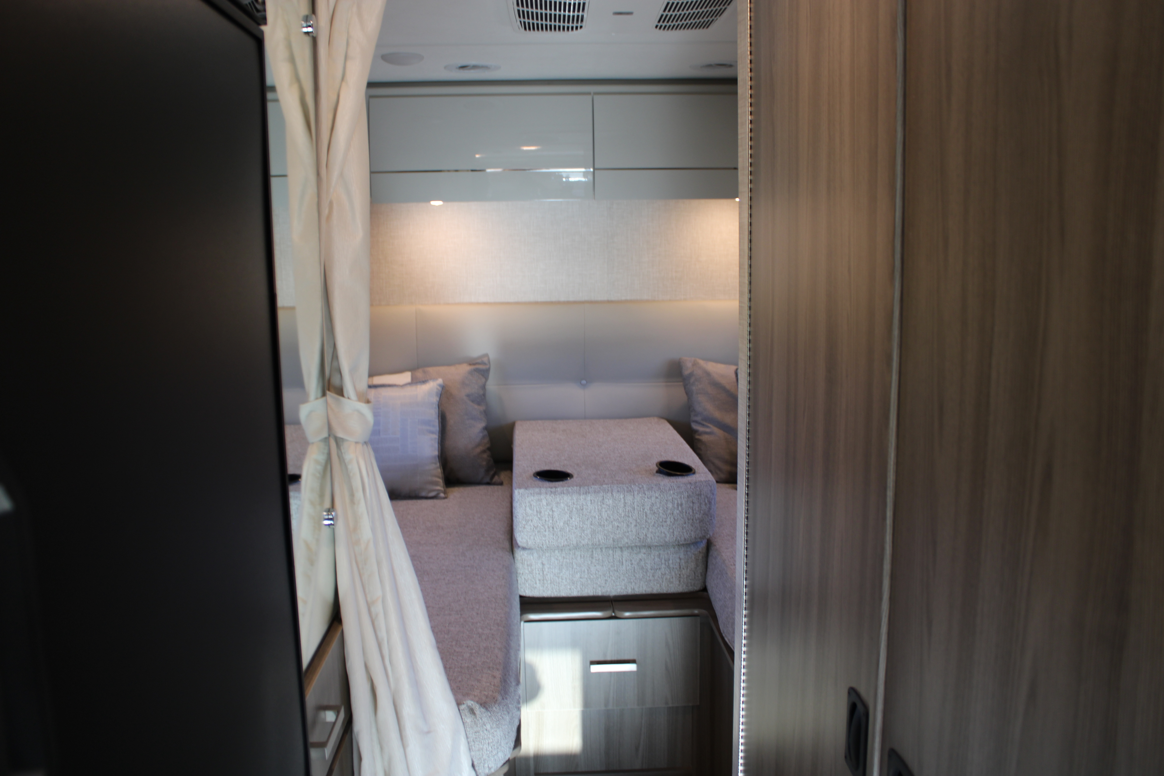 Cozy interior of an RV rental bedroom with modern furnishings, overhead cabinets, and built-in cup holders.. Ford Thor Gemini 24KB 2025