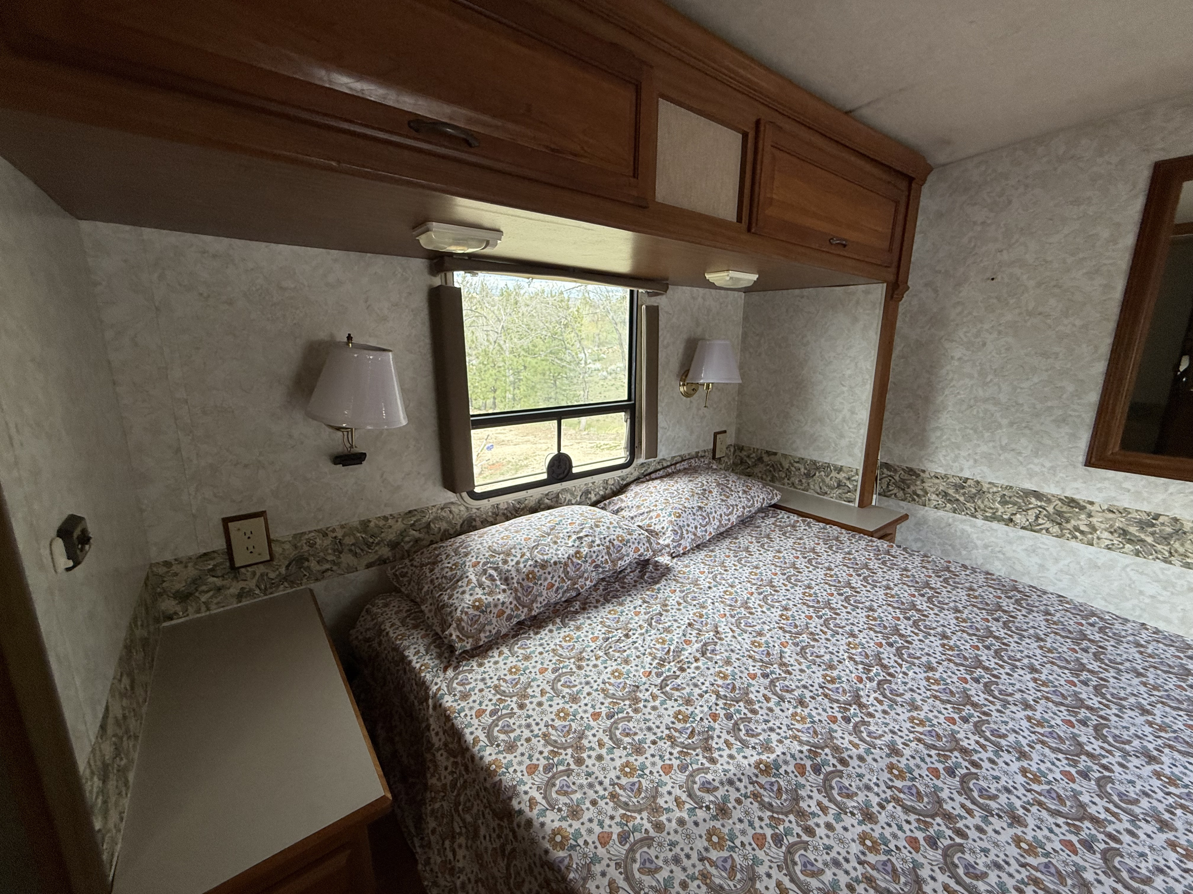 An RV rental bedroom, featuring a large bed with floral and mushroom bedding, built-in cabinets, and window.. Winnebago Chieftain 1999