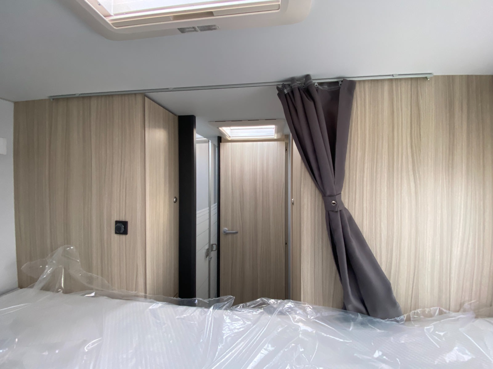 RV rental interior featuring a bedroom with a new bed, tied-back gray curtain, and a central doorway leading to a bathroom.. SunLiving S 70 SP 2025