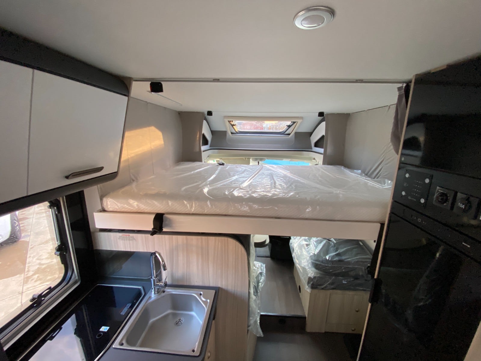 Explore this new rv rental interior featuring an elevated main bed, kitchenette with sink, and flexible rear sleeping space.. SunLiving S 70 SP 2025