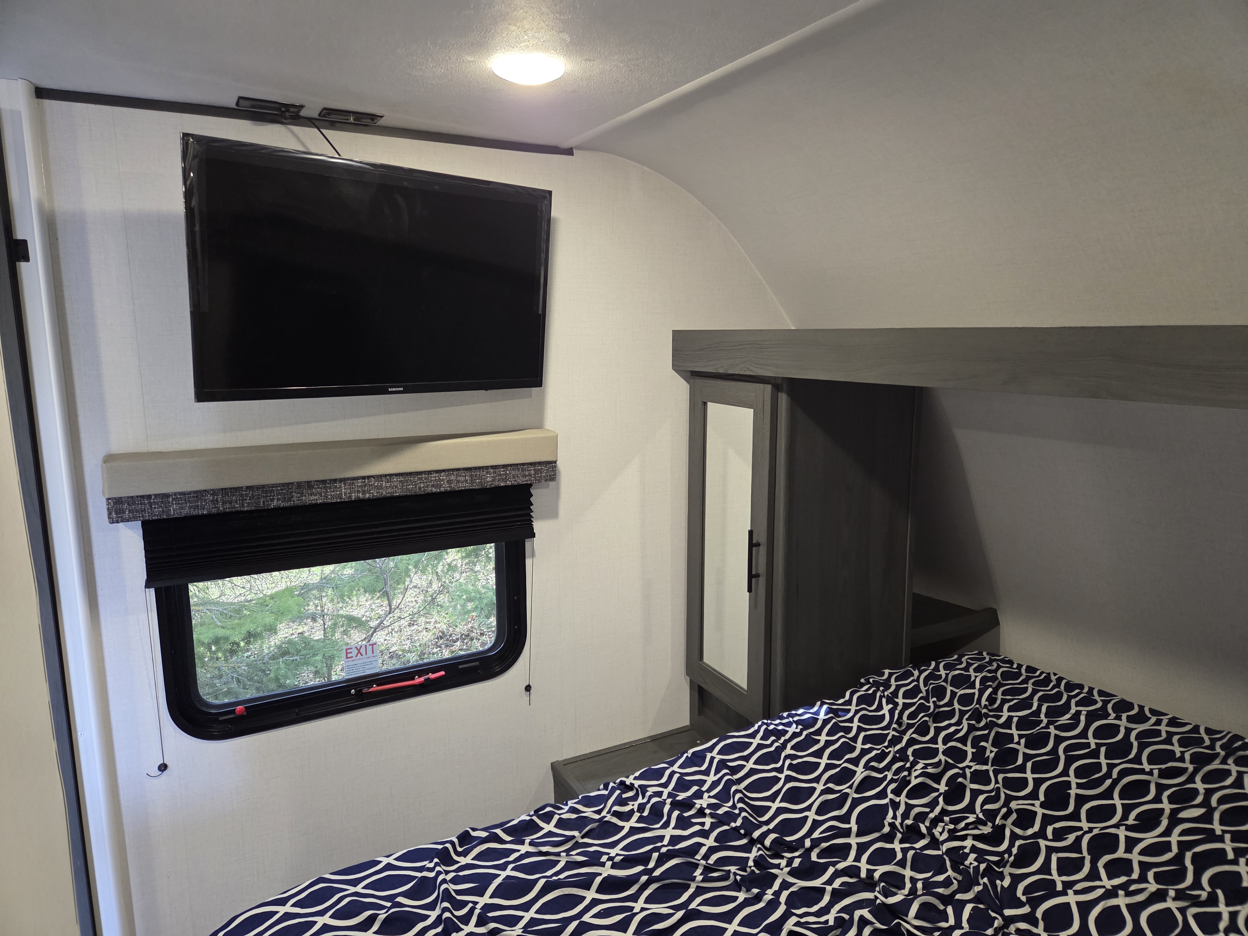 View inside an RV rental bedroom showing a bed with patterned bedding, wall-mounted TV, window, and storage.. Dutchmen Aspen Trail 2025