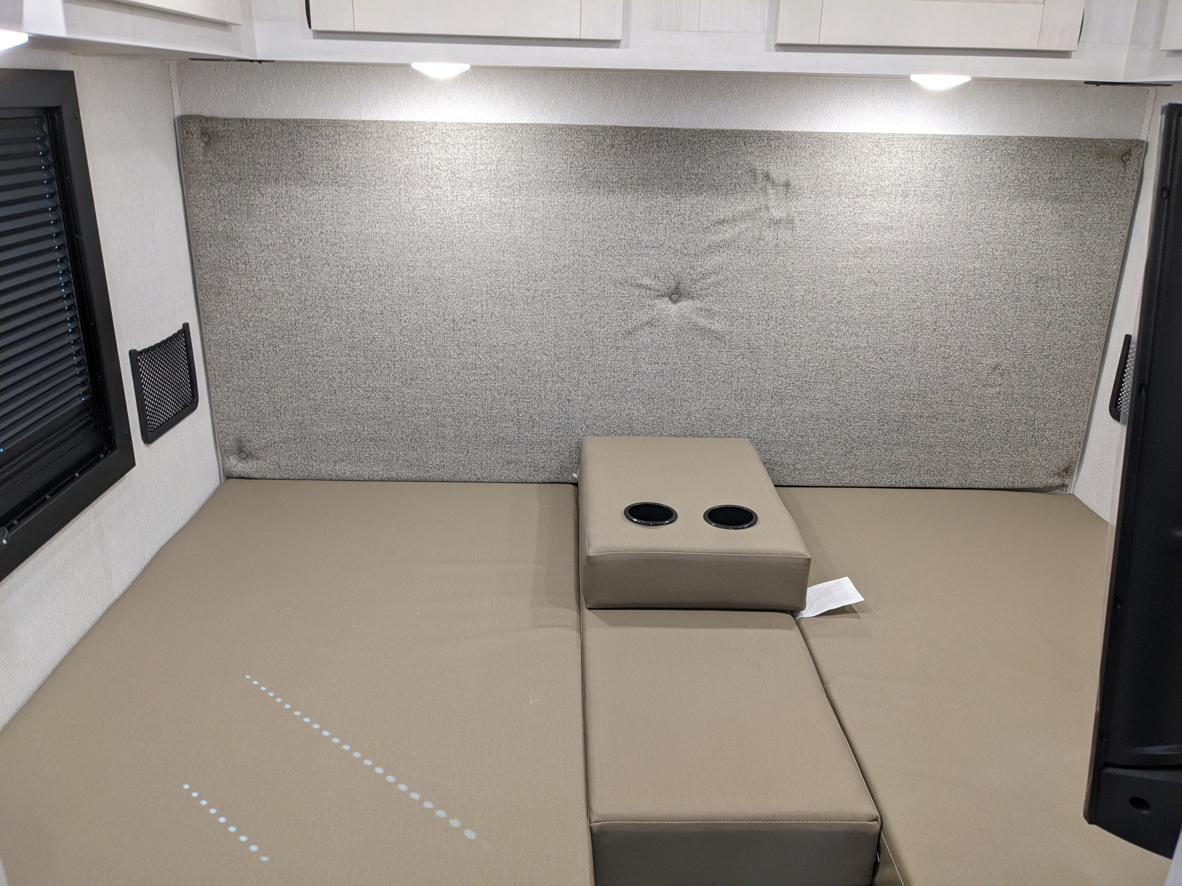 Comfortable RV rental interior featuring a versatile upholstered bed/lounge area with integrated cupholders, overhead lighting, and storage.. East to West Alita 2025