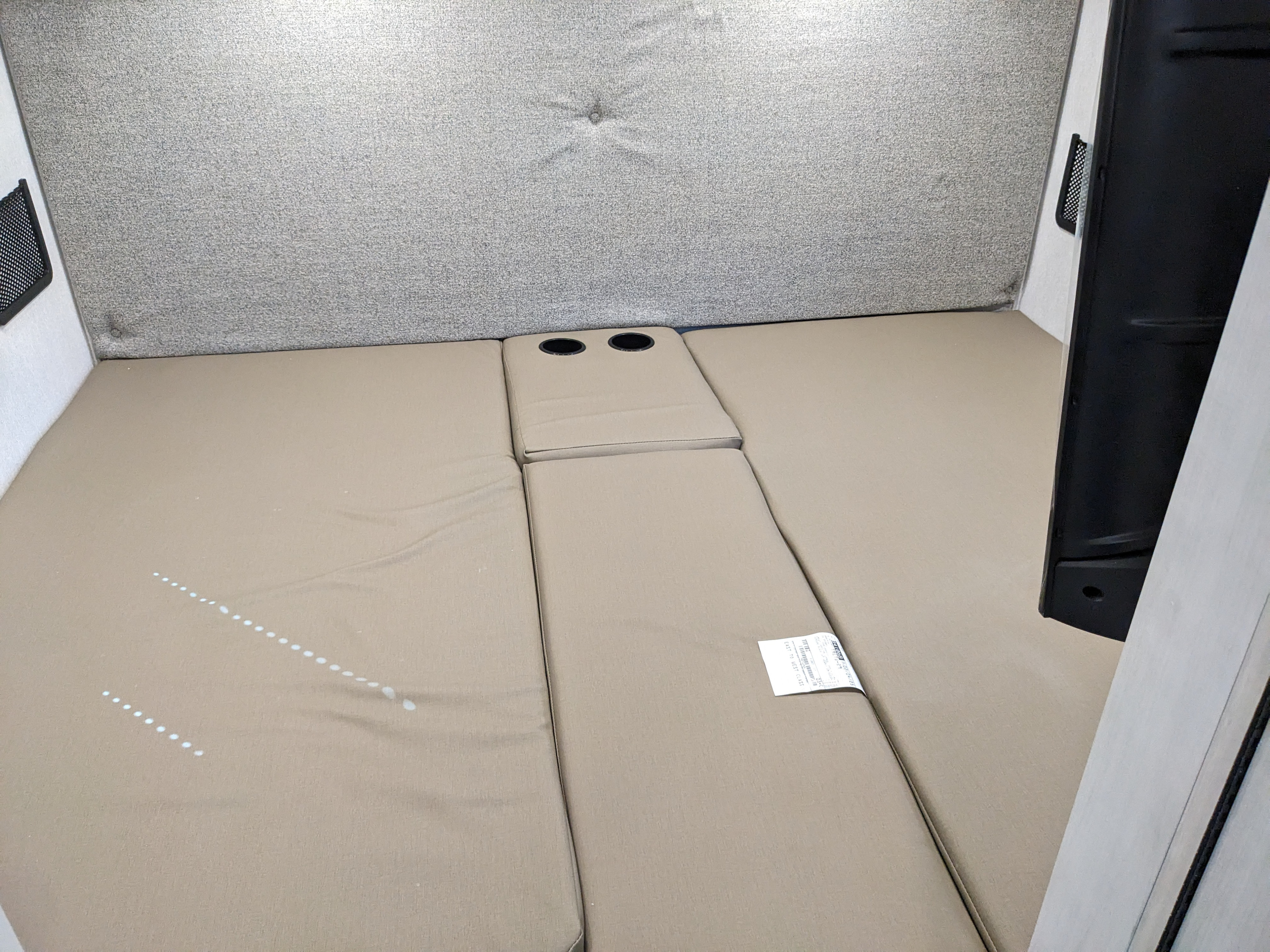 Inside an RV rental: a comfortable bed area with tan cushions and integrated cup holders, ready for your travels.. East to West Alita 2025