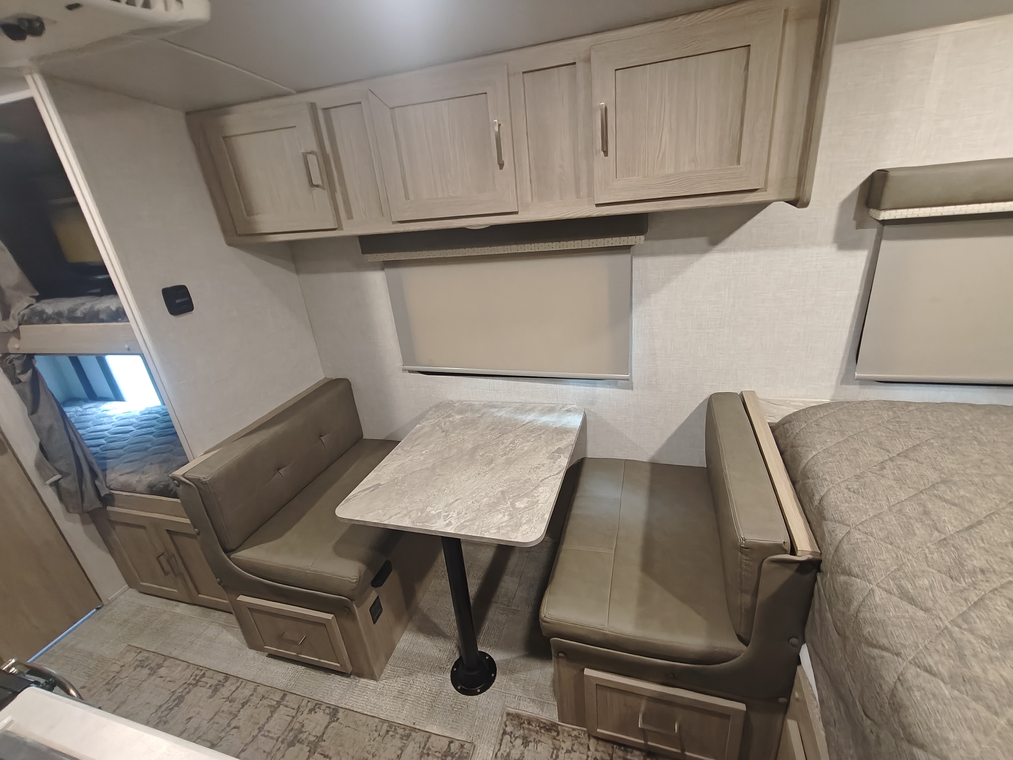 This RV rental interior features a dinette, bunk beds, overhead cabinets, and a main bed, showcasing compact living.. Geopro 19Bh 2021