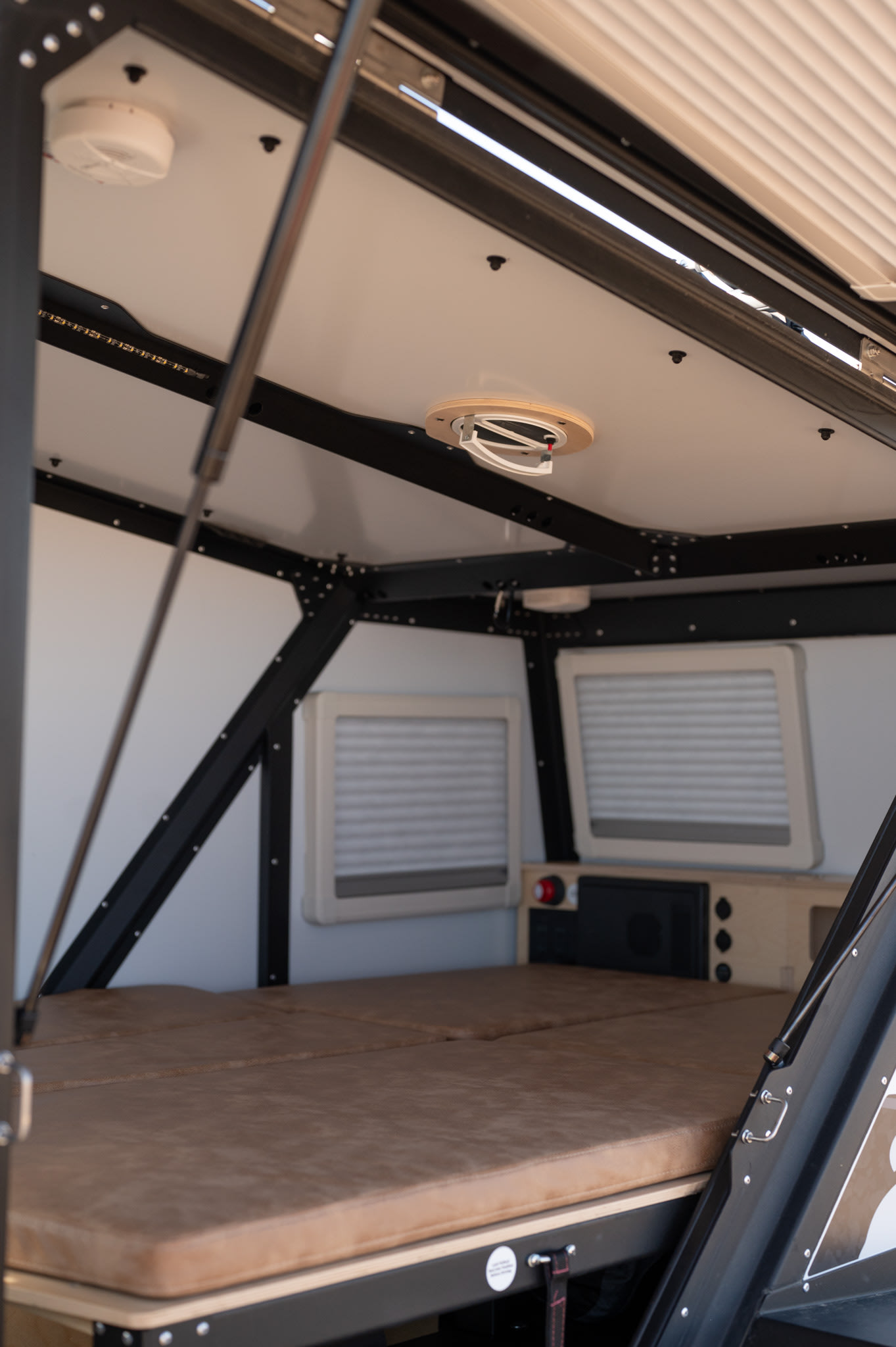 Cozy RV rental interior with a comfortable bed, small windows, and an overhead fan, ready for your next adventure.. TAXA Tiger Moth 2023