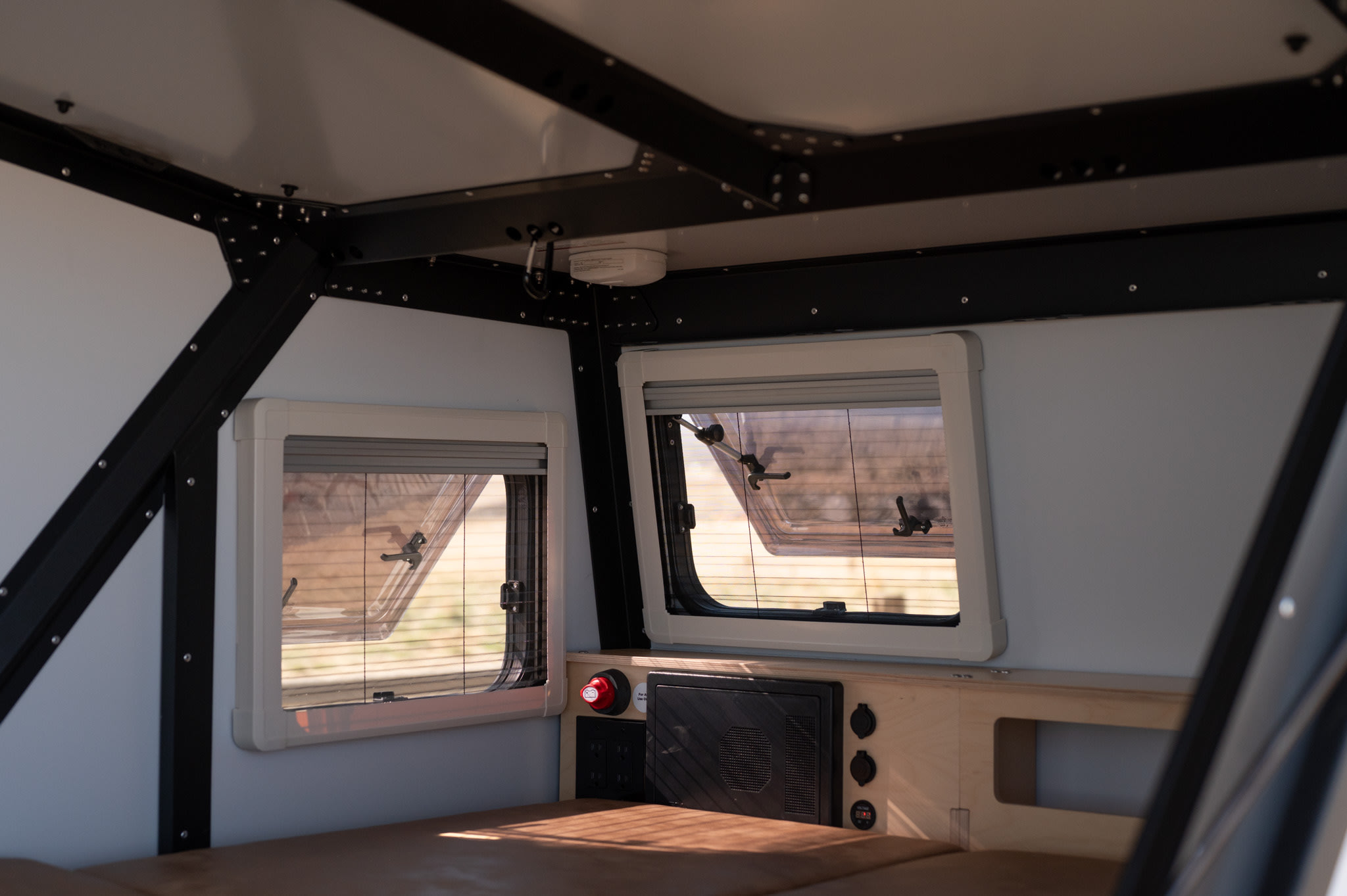 Interior of an RV rental: well-appointed space with large windows, power hub, and comfy sleeping area.. TAXA Tiger Moth 2023